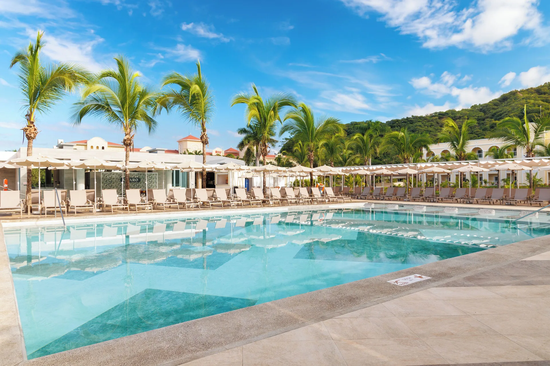 Large resort pool with loungers, umbrellas and palm trees at Hotel Riu Guanacaste.