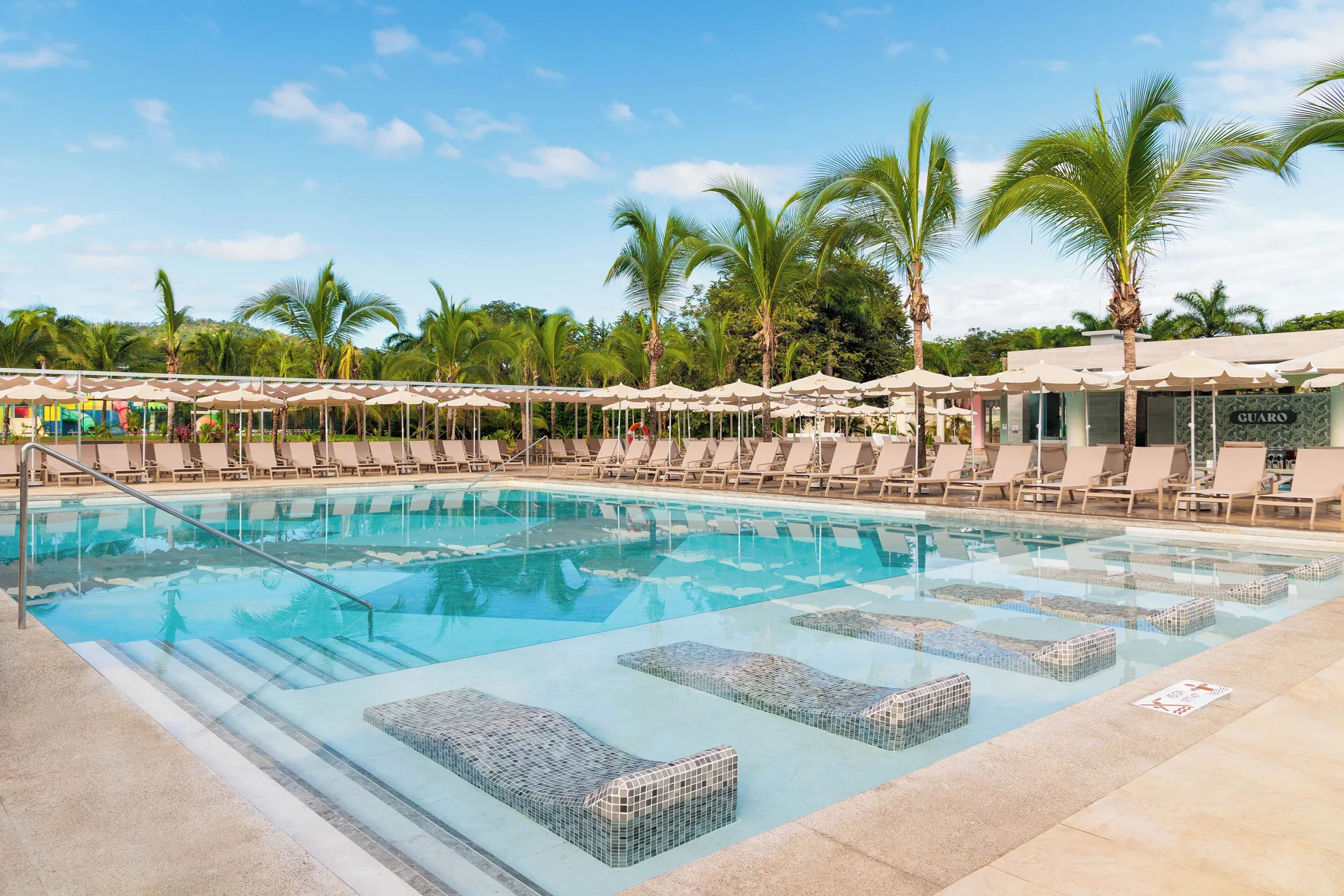 Pool with submerged loungers, umbrellas and palm trees at Hotel Riu Guanacaste.