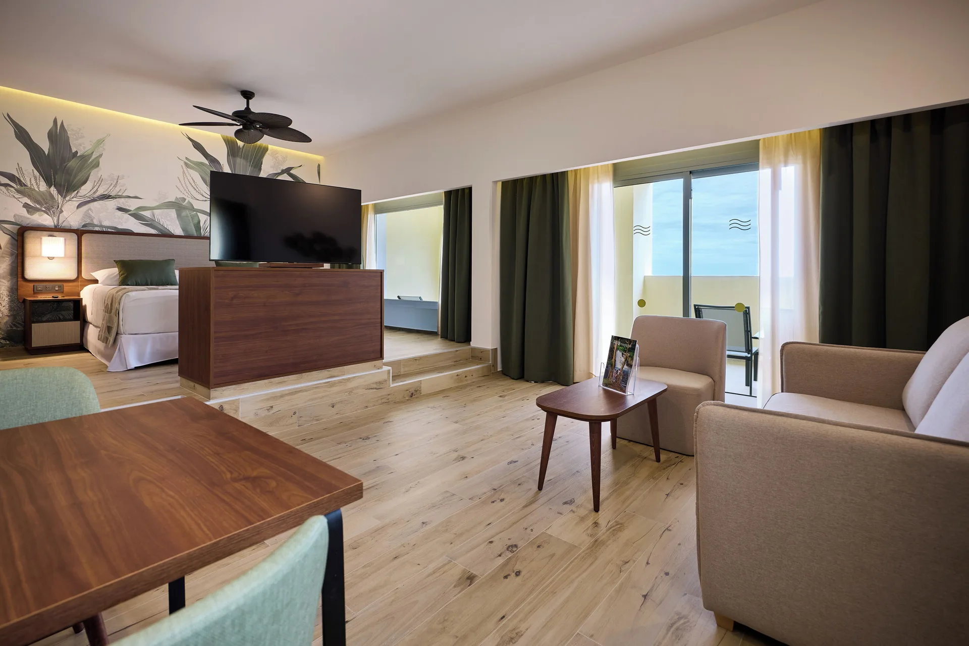 Suite living area with sofa, dining table, TV, bed alcove and balcony at Hotel Riu Guanacaste.