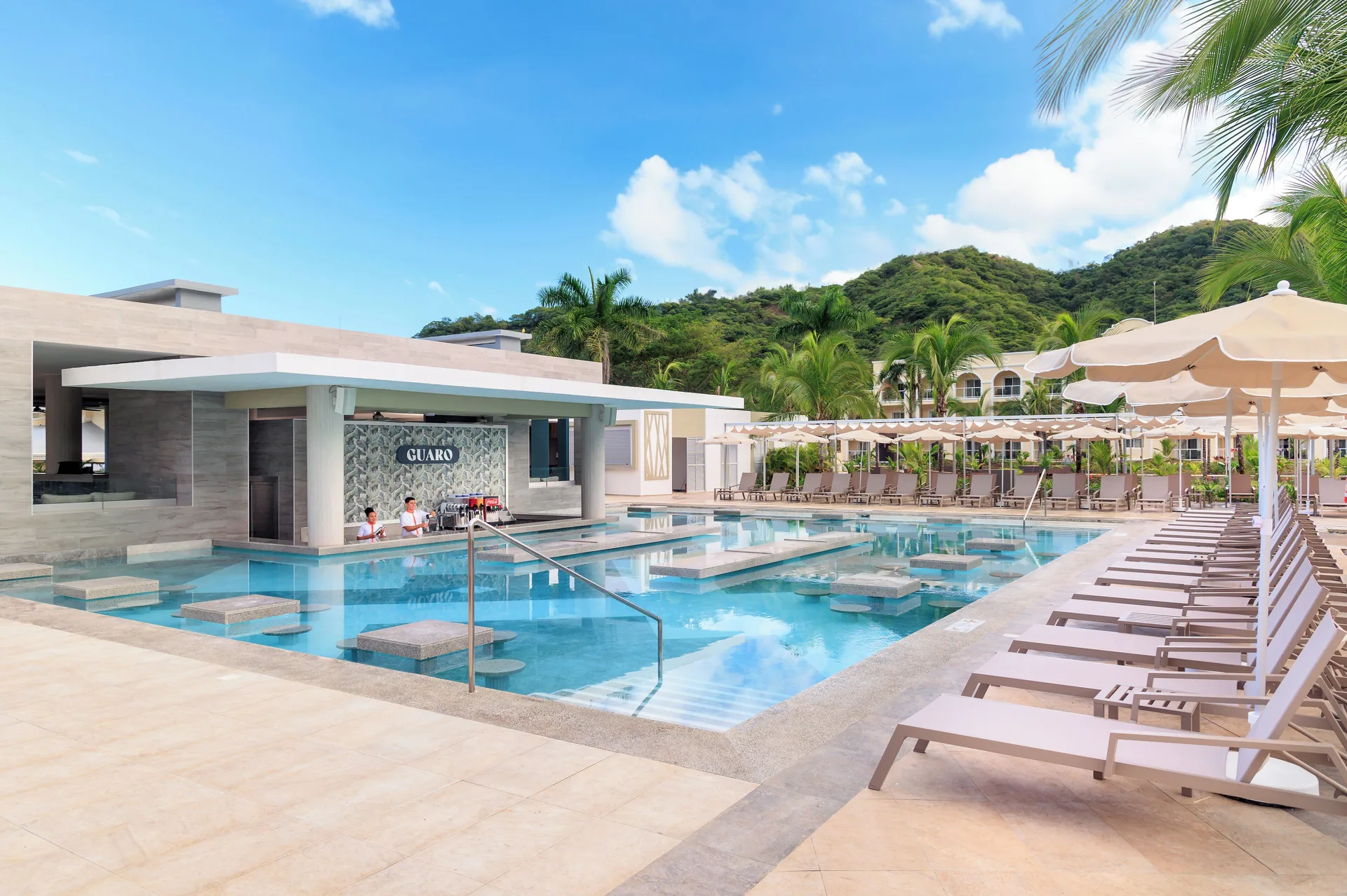 Pool bar area with loungers, umbrellas, palms and hillside backdrop at Hotel Riu Guanacaste.