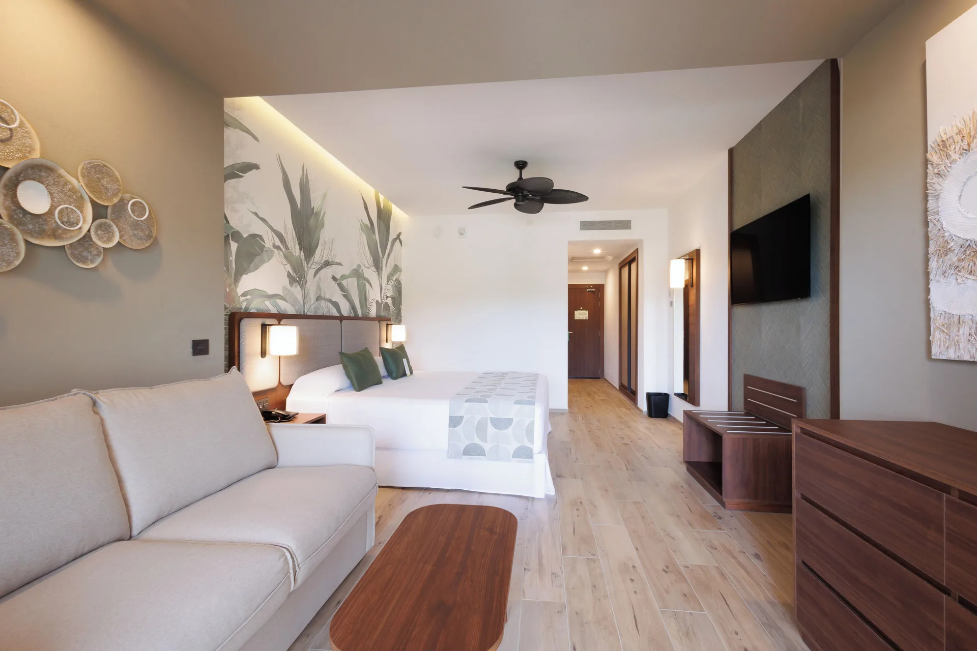 Deluxe Room with sofa, bed, TV and wood furniture at Hotel Riu Guanacaste.