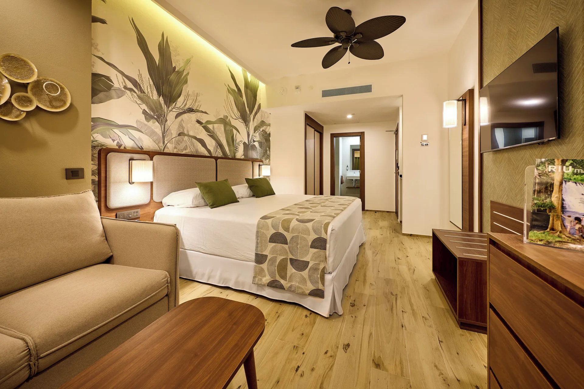 Guest room with king bed, sofa, TV, and tropical wall art at Hotel Riu Guanacaste.