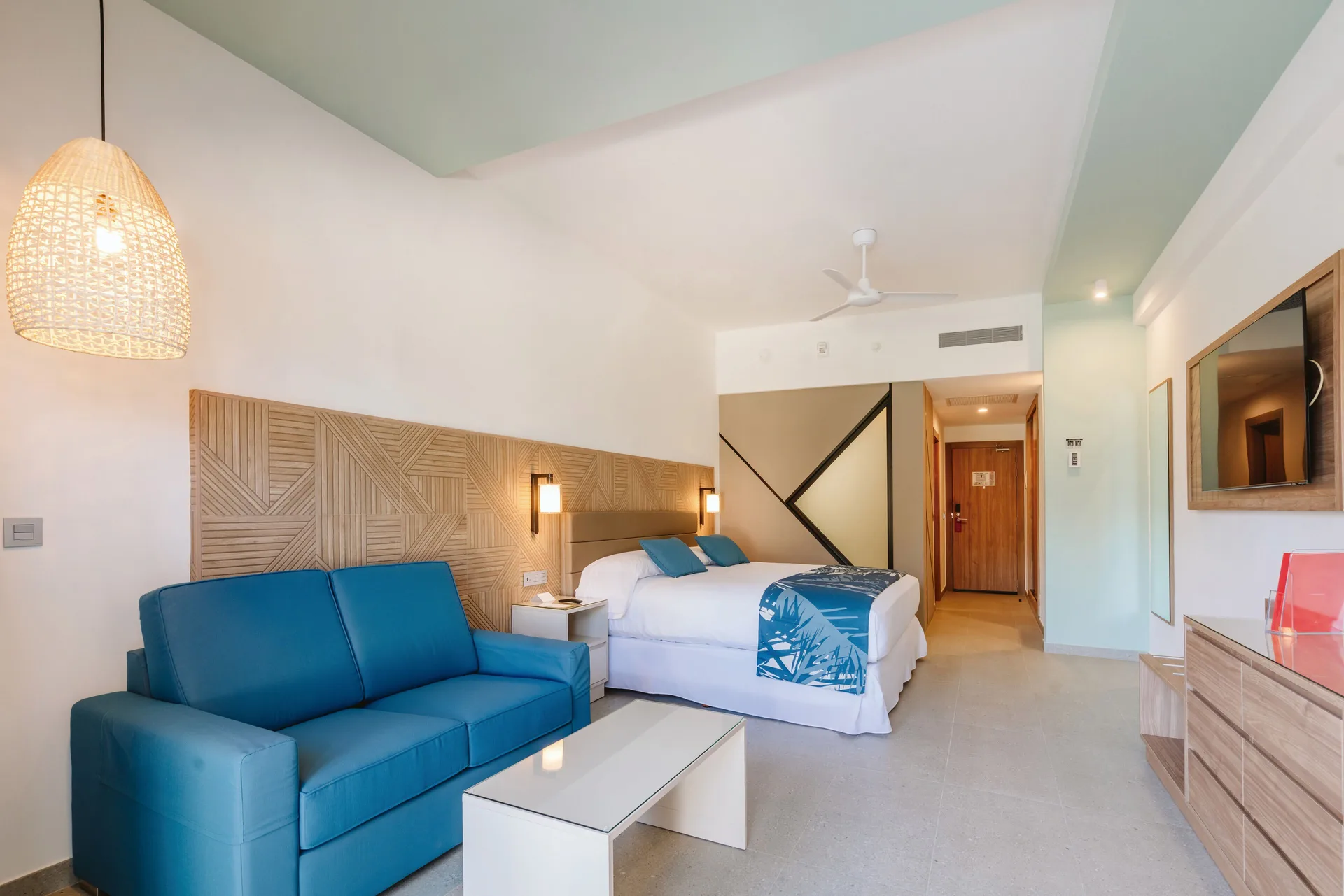 Ocean View Standard Room seating area with blue sofa and king bed at Hotel Riu Latino.