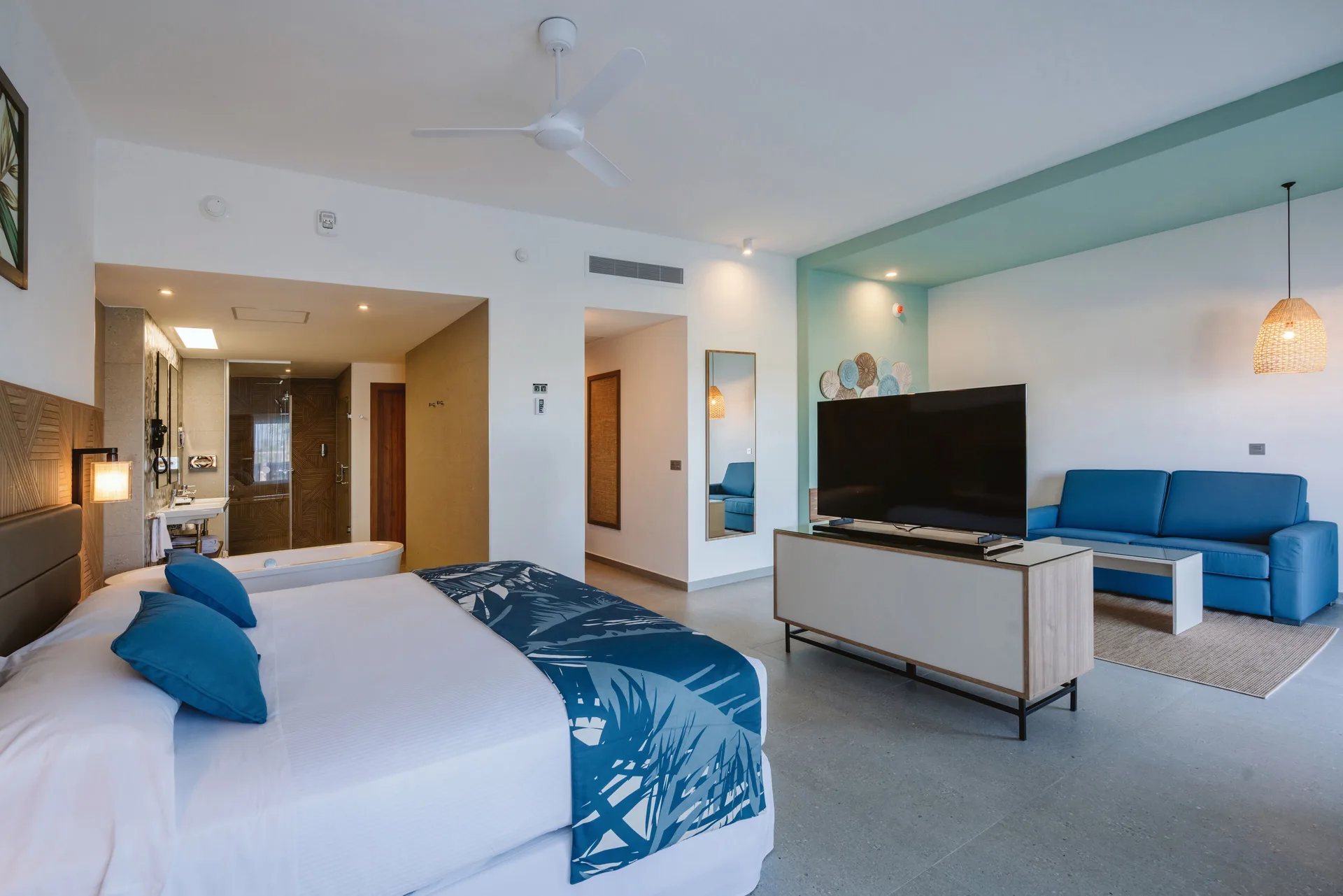 Ocean View Suite at Hotel Riu Latino with king bed, bathtub, TV, and blue sofa seating area.