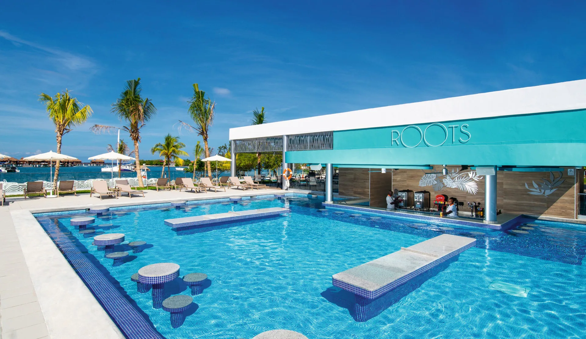 Swim-up pool bar at Hotel Riu Montego Bay with stools, tables and a turquoise facade.