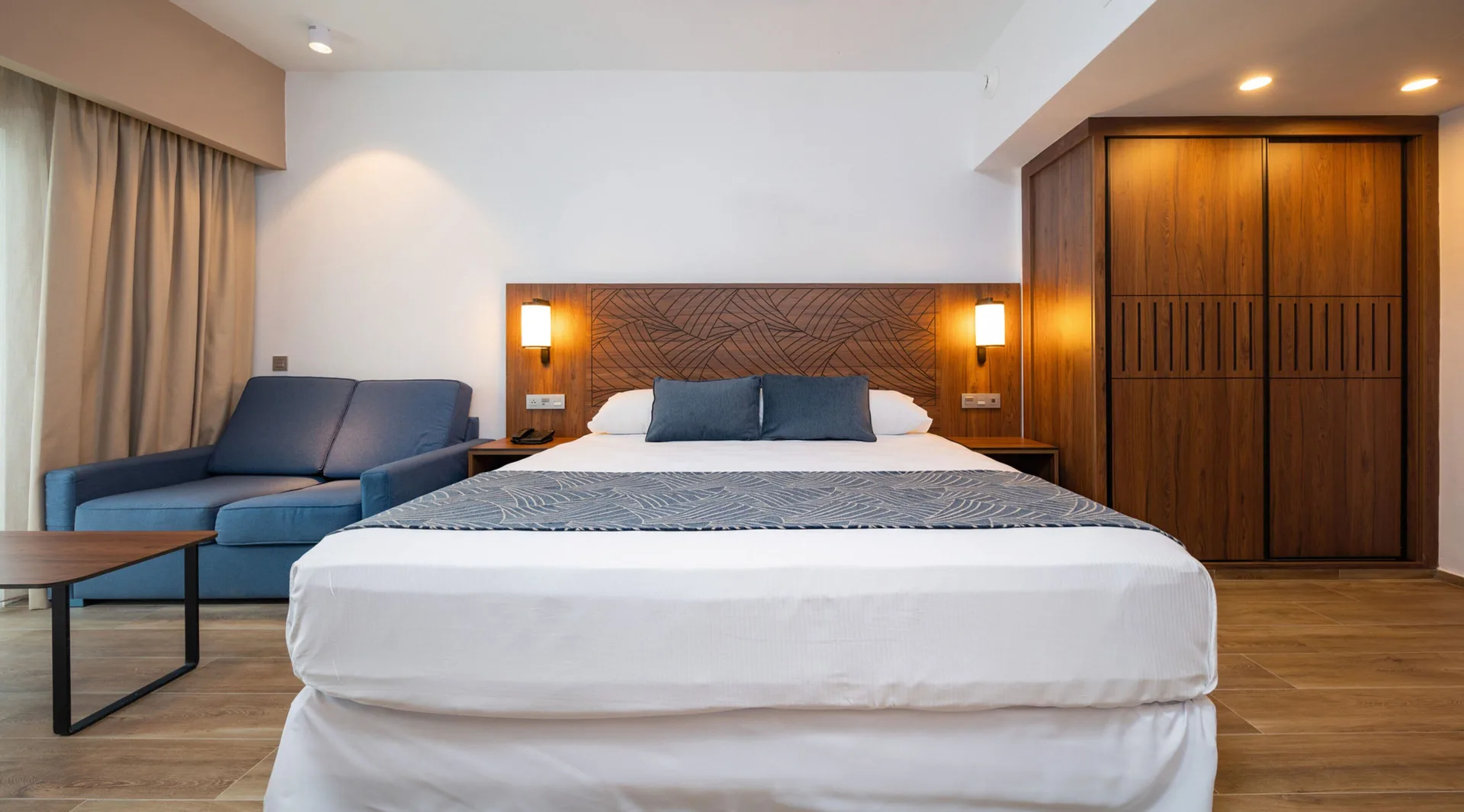 Guest room with king bed, blue sofa and wood wardrobe at Hotel Riu Montego Bay.