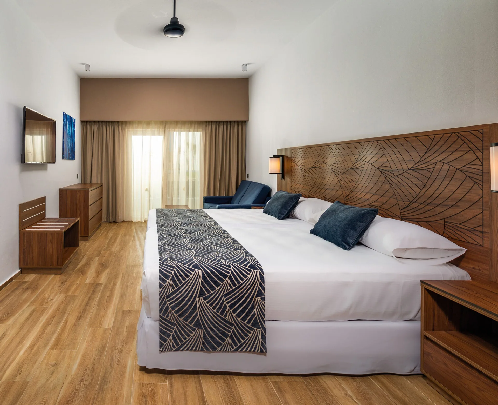 Guest room with king bed, dresser, wall-mounted TV and balcony curtains at Hotel Riu Montego Bay.