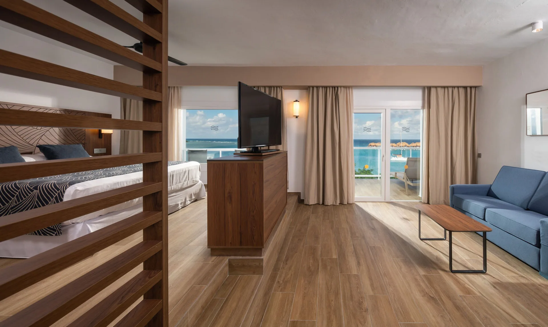 Suite Ocean View sitting area with sofa, TV, balcony, and bed at Hotel Riu Montego Bay.