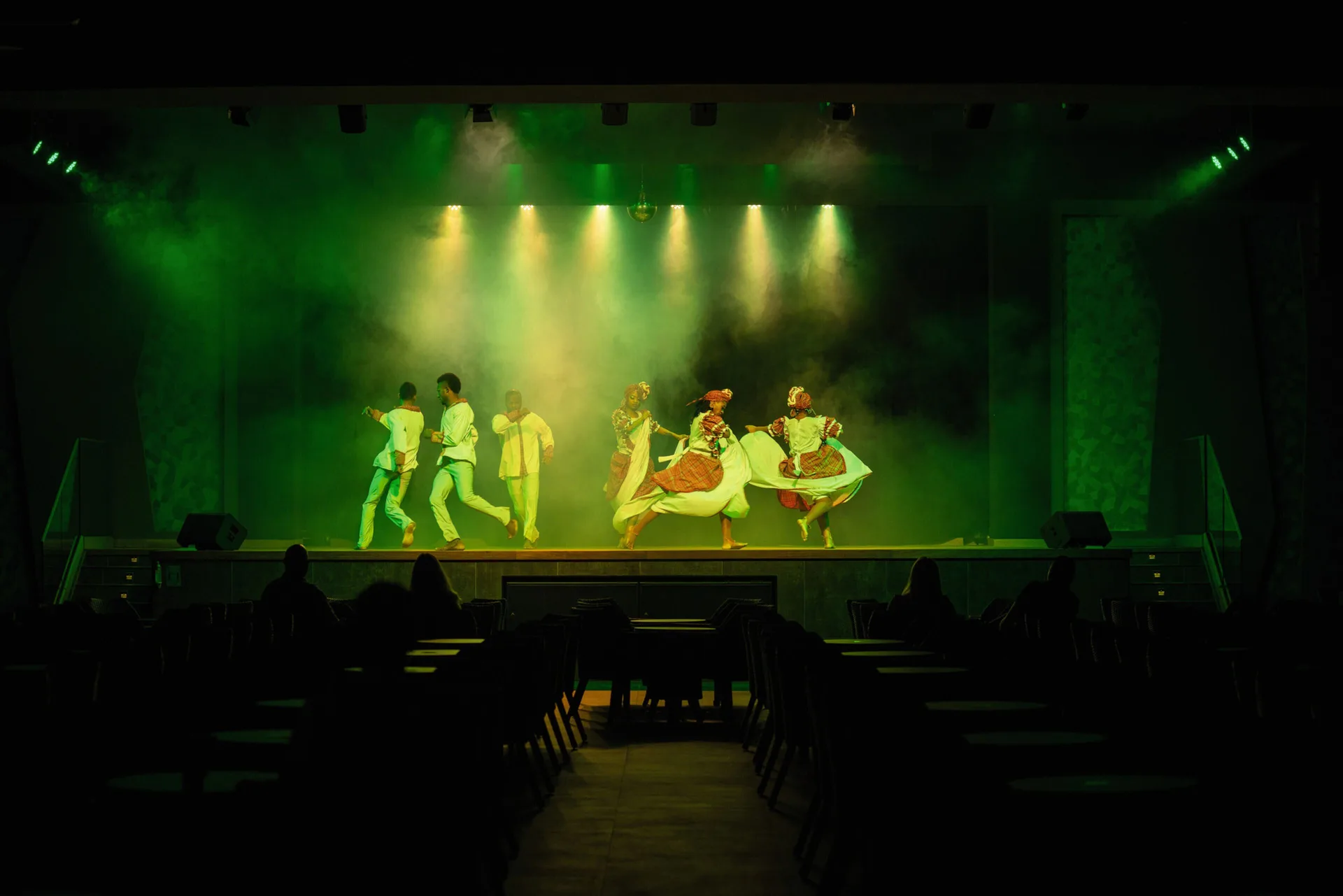 Dancers performing on a smoky green-lit theater stage at Hotel Riu Montego Bay.