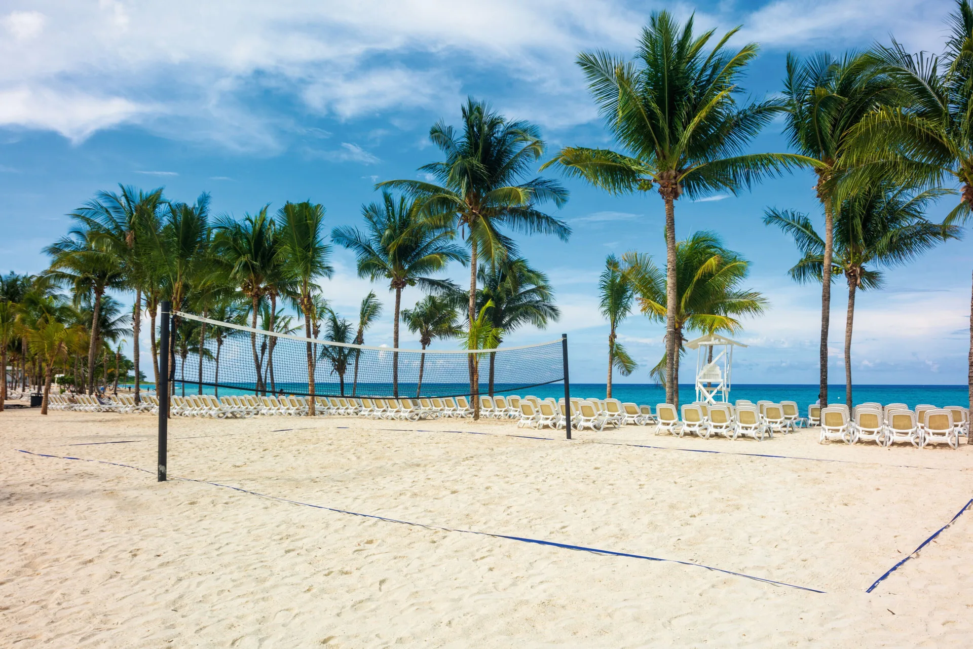 Beach volleyball net, palm trees, loungers, and blue sea at Hotel Riu Ocho Rios.