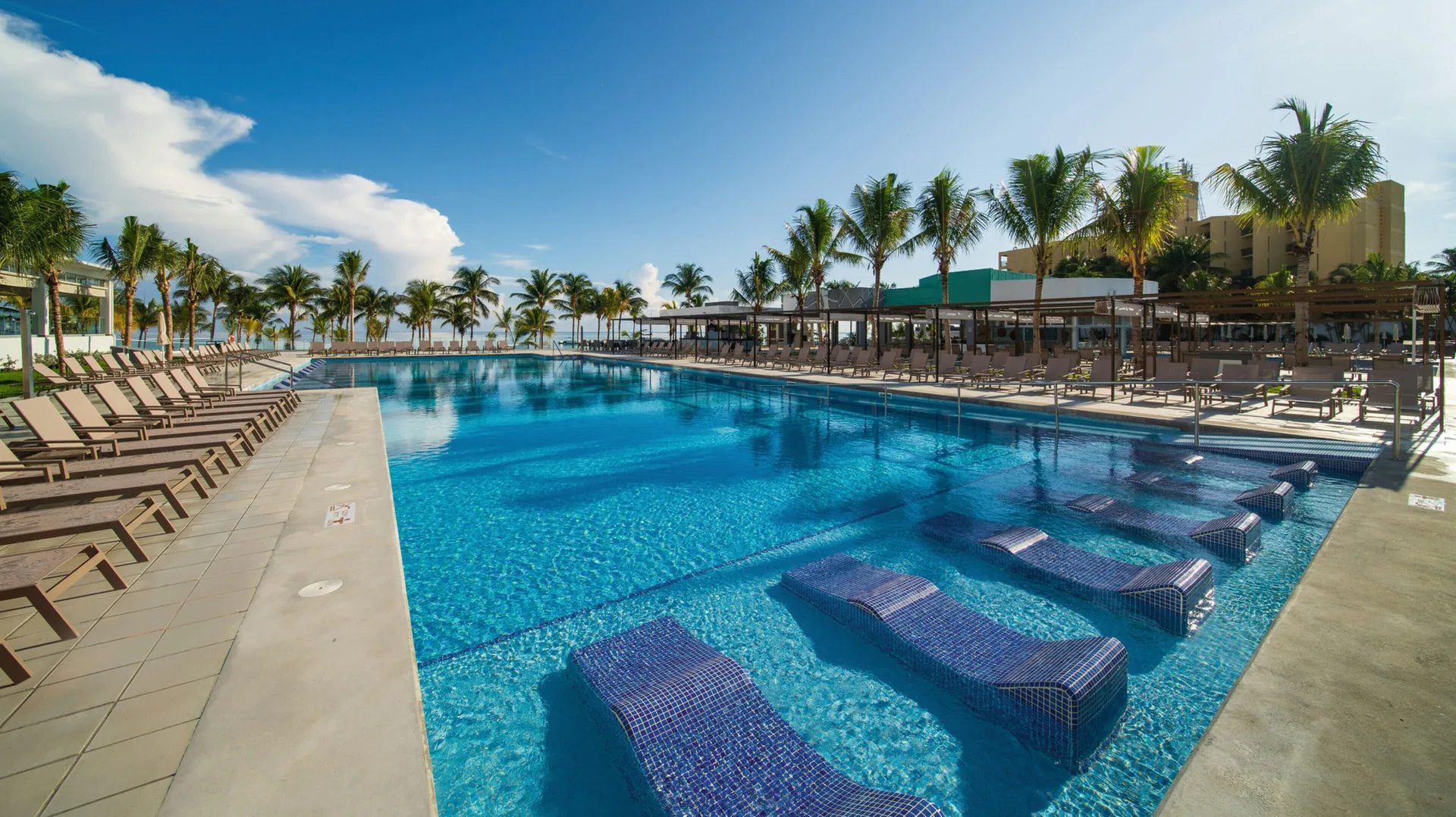 Large pool with submerged loungers and palm trees at Hotel Riu Ocho Rios.