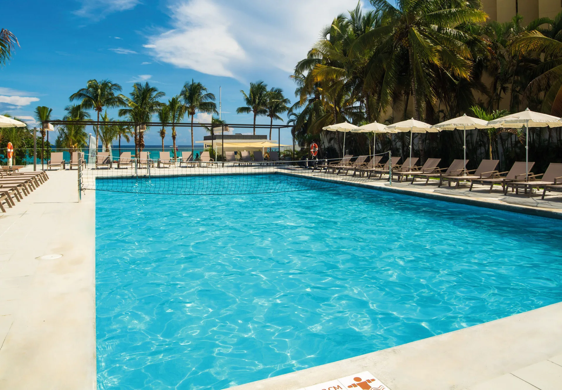 Pool with volleyball net, lounge chairs, and ocean backdrop at Hotel Riu Ocho Rios.