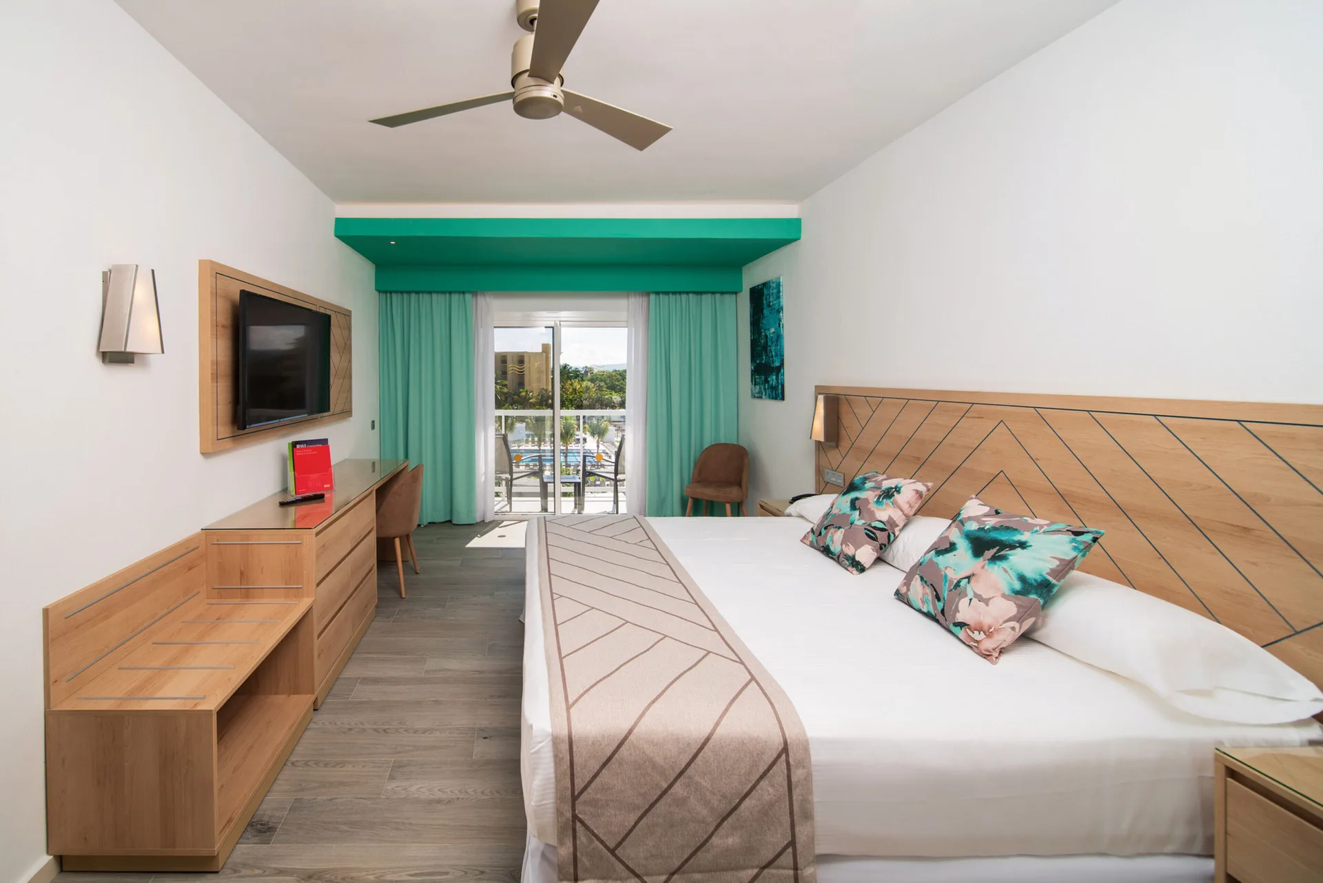 Ocean View room with a large bed, desk, TV, balcony doors, and partial outdoor view at Hotel Riu Ocho Rios.