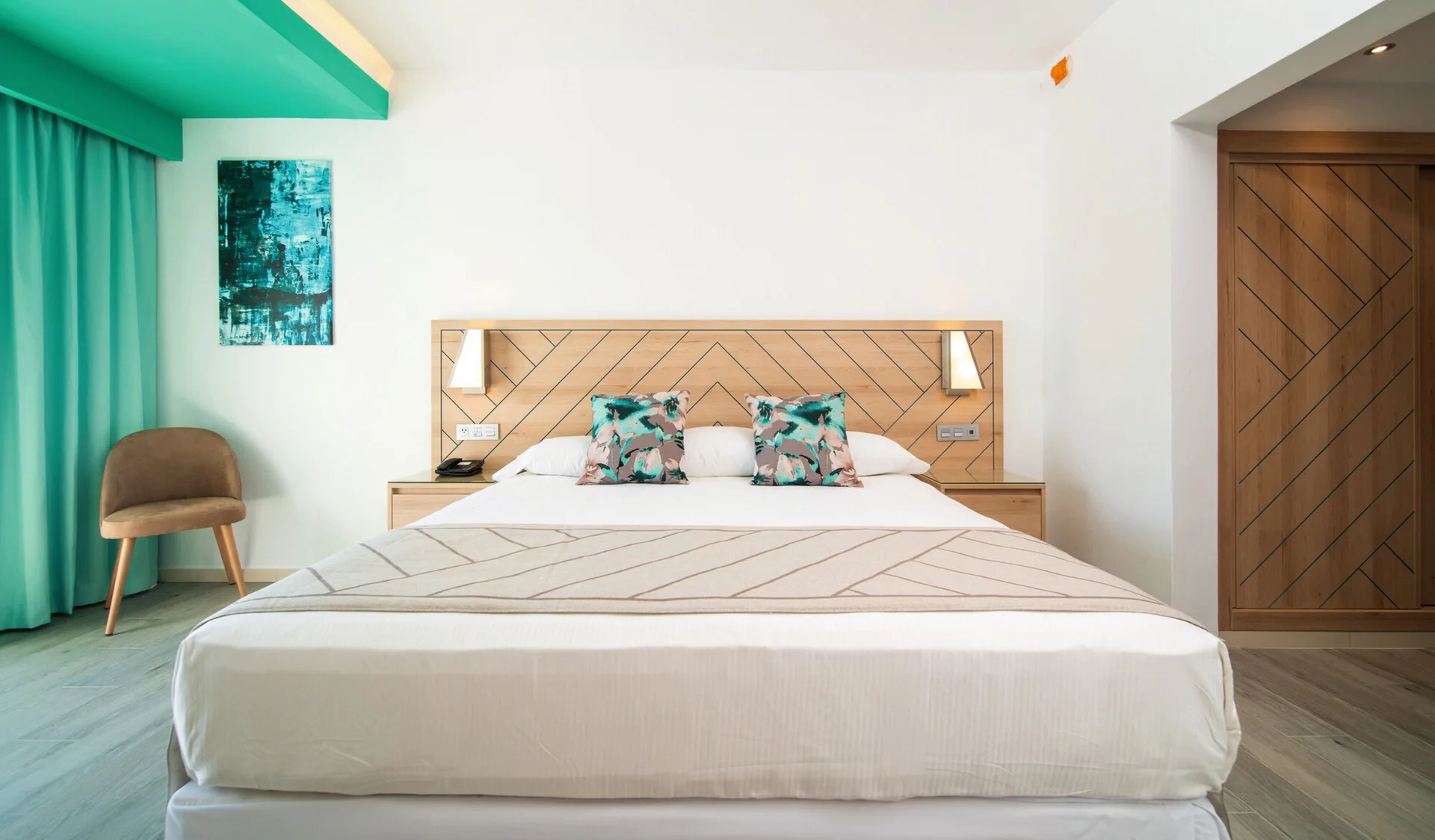 Ocean View room bed with turquoise curtains, bedside lights, and wardrobe at Hotel Riu Ocho Rios.