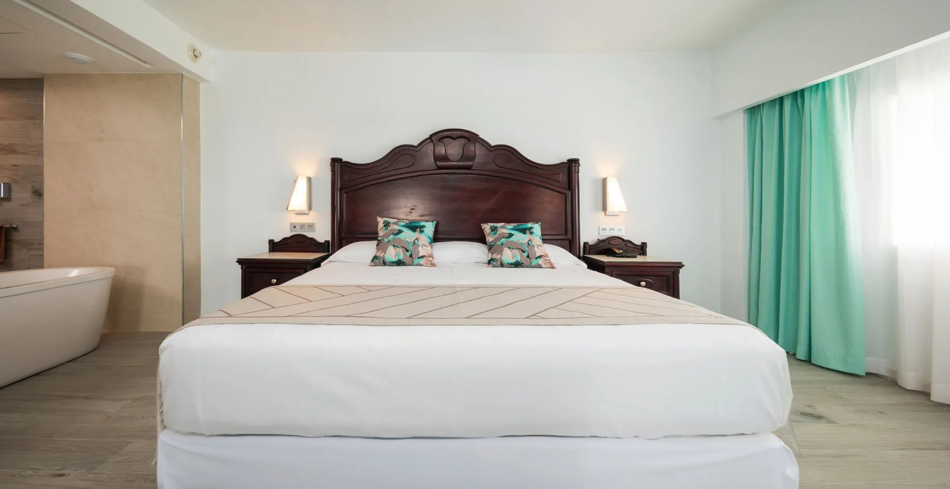 Ocean View Suite king bed with bedside tables, lamps and curtains at Hotel Riu Ocho Rios.