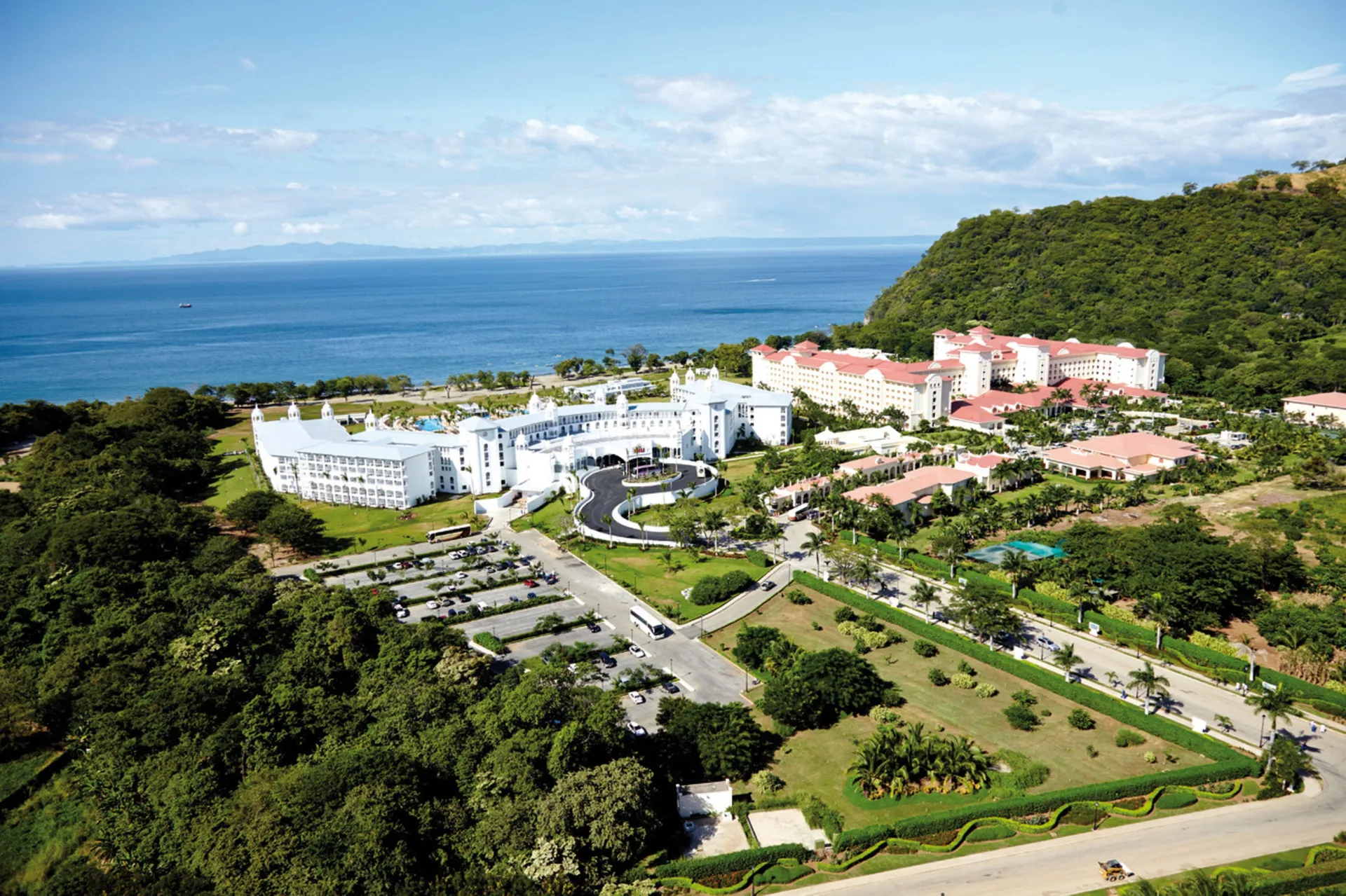 Aerial view of Hotel Riu Palace Costa Rica between green hills and the ocean.