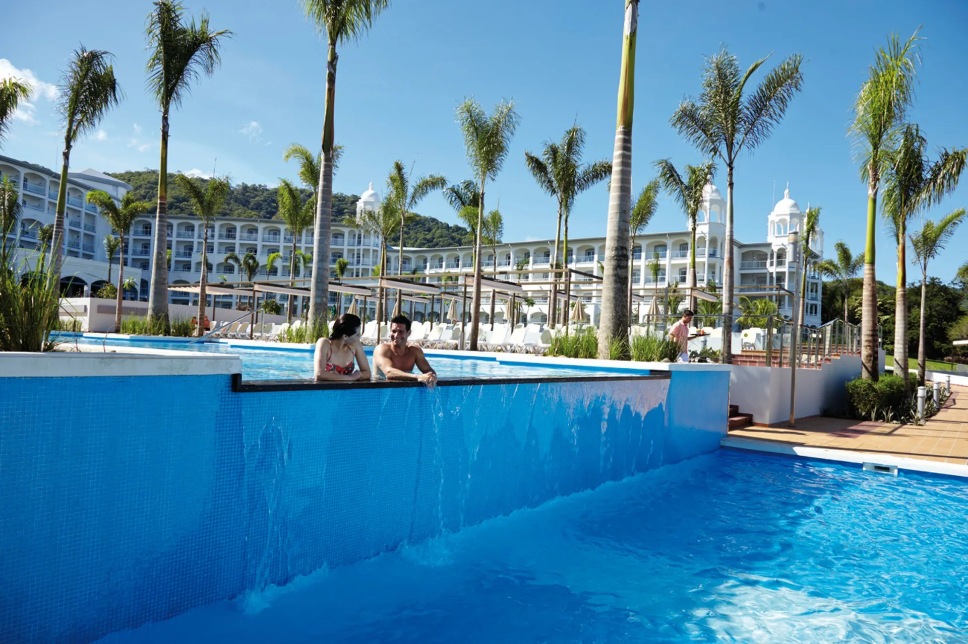 Guests at an elevated pool edge with palms at Hotel Riu Palace Costa Rica.