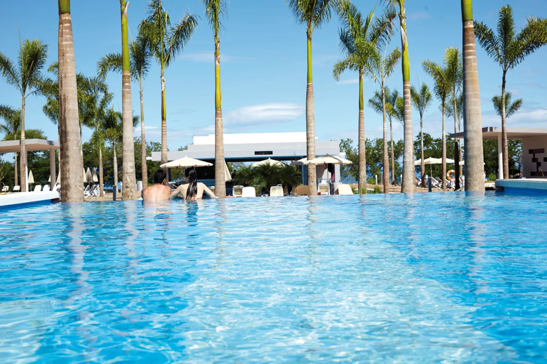 Guests in a palm-lined swimming pool at Hotel Riu Palace Costa Rica.