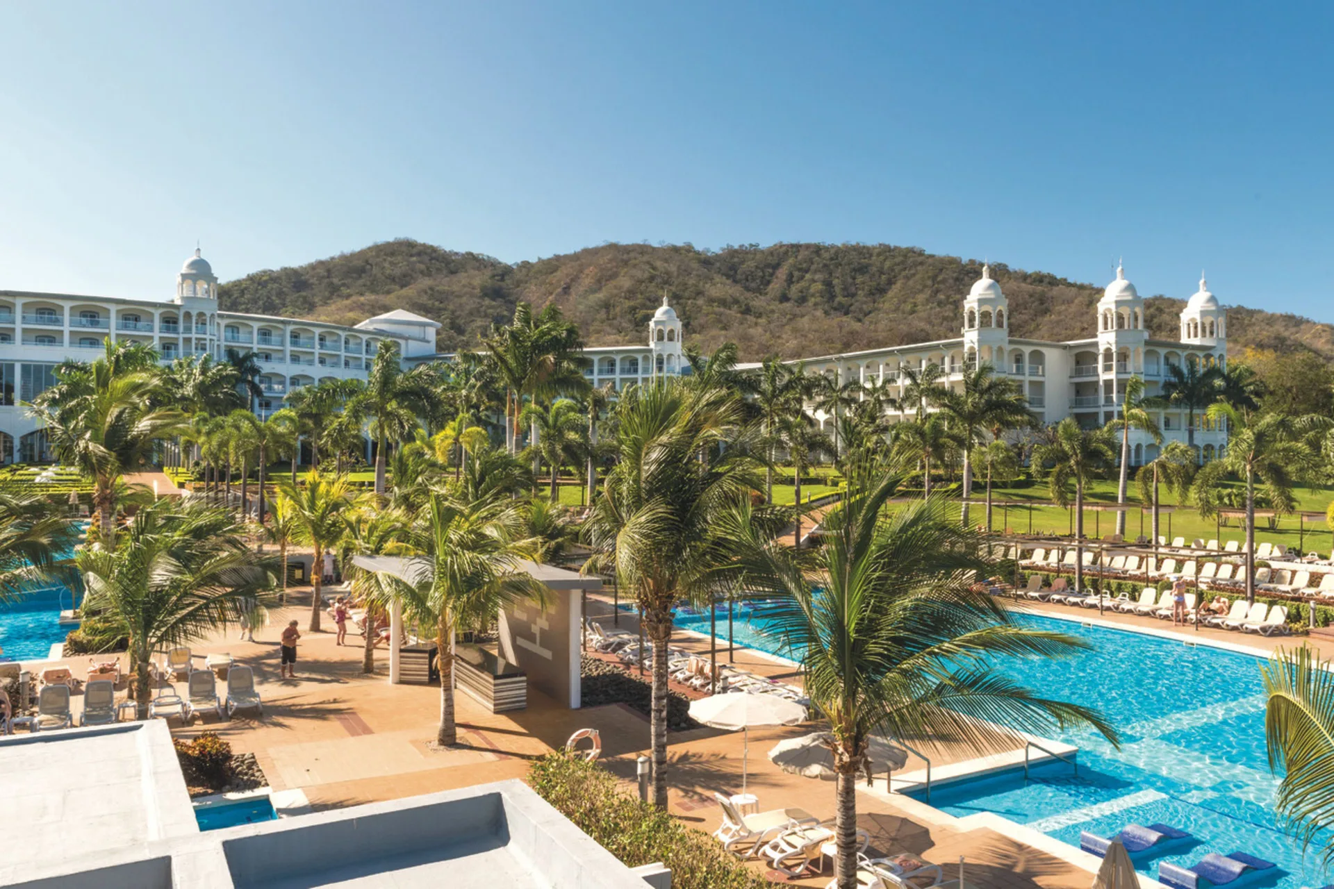 Pool area with palms and resort buildings at Hotel Riu Palace Costa Rica.