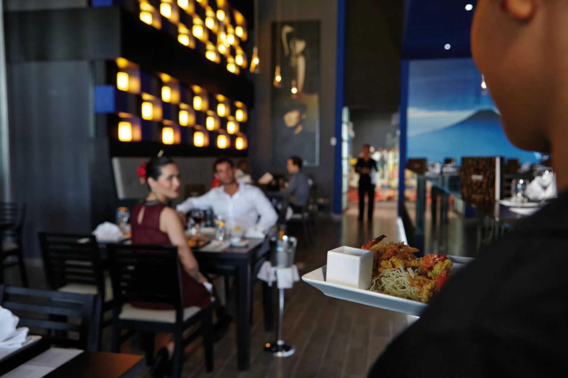 A server carries a plated dish through a dim dining room at Hotel Riu Palace Costa Rica.