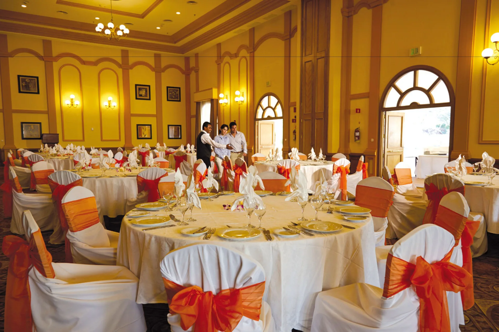 A banquet room set with round tables and orange chair sashes at Hotel Riu Palace Costa Rica.