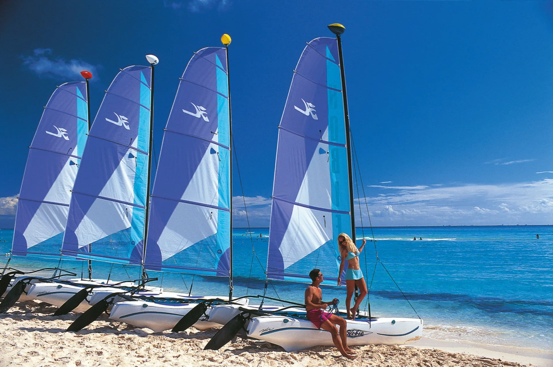 Catamarans with blue sails line the beach at Hotel Riu Palace Peninsula.