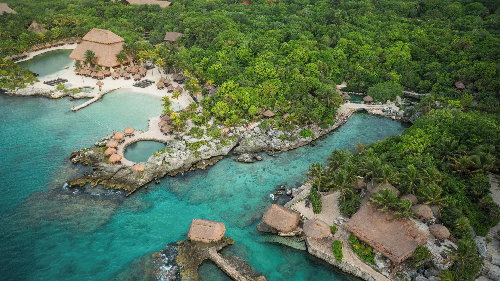 Aerial view of turquoise coves, thatched roofs, and jungle near Hotel Xcaret Arte.
