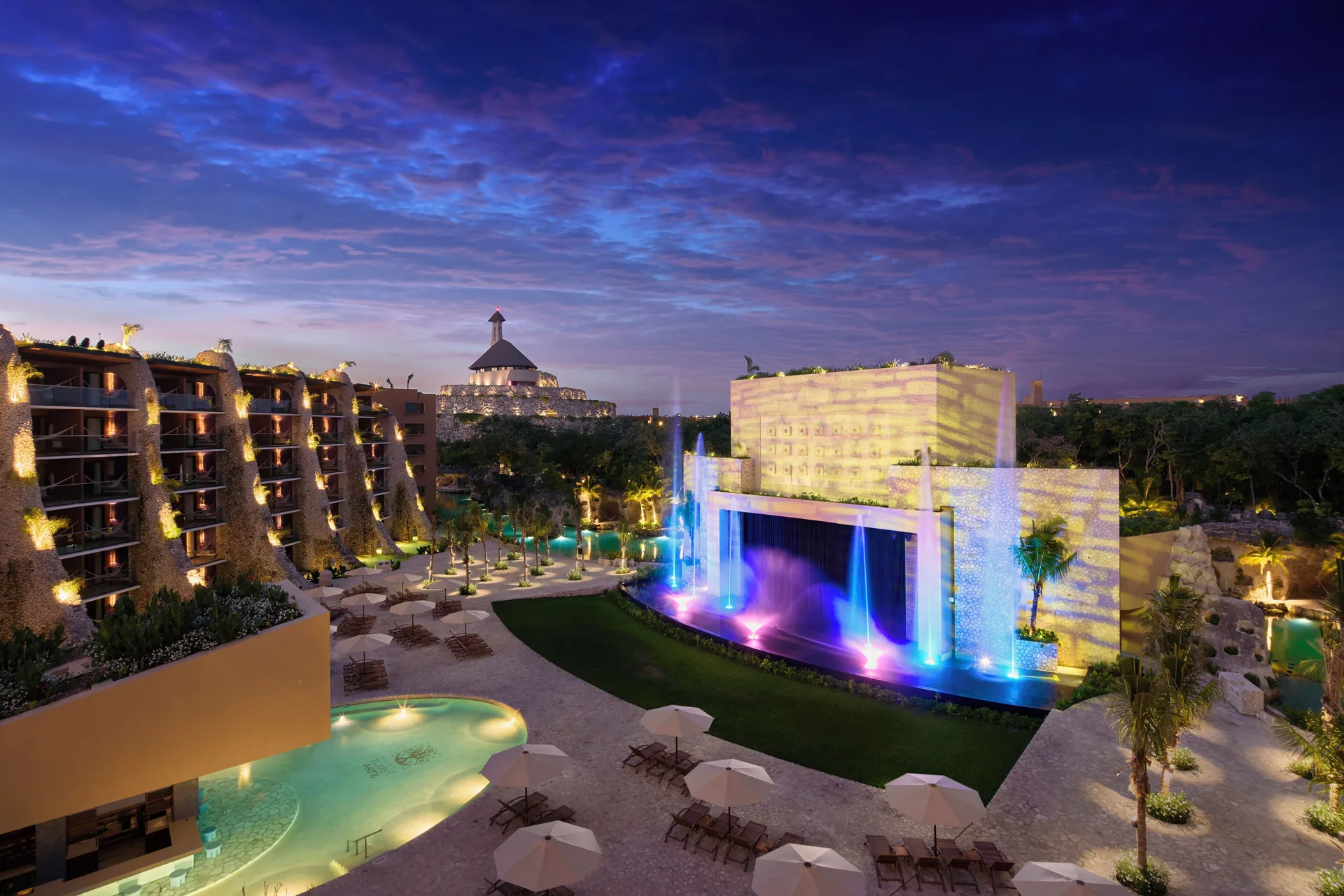 Resort courtyard with pools, lounge chairs, and colorful fountains at Hotel Xcaret Arte.