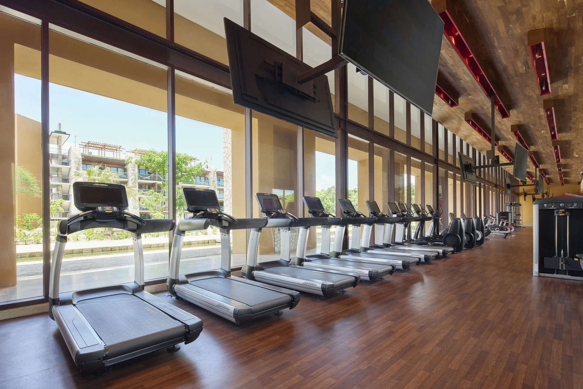 Fitness center treadmills lined up by tall windows at Hotel Xcaret Arte.