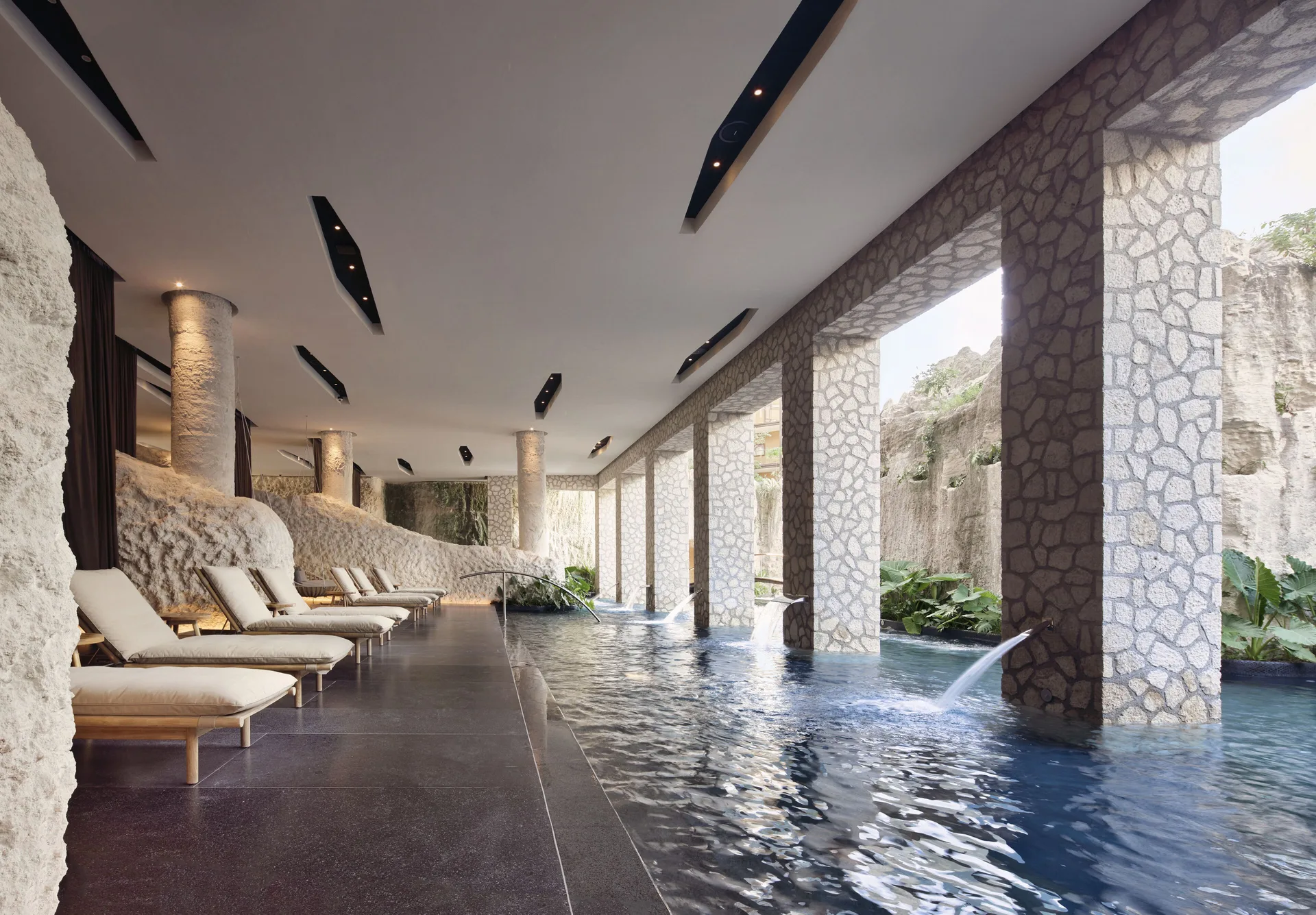 Indoor spa pool with loungers, stone columns, and water jets at Hotel Xcaret Arte.