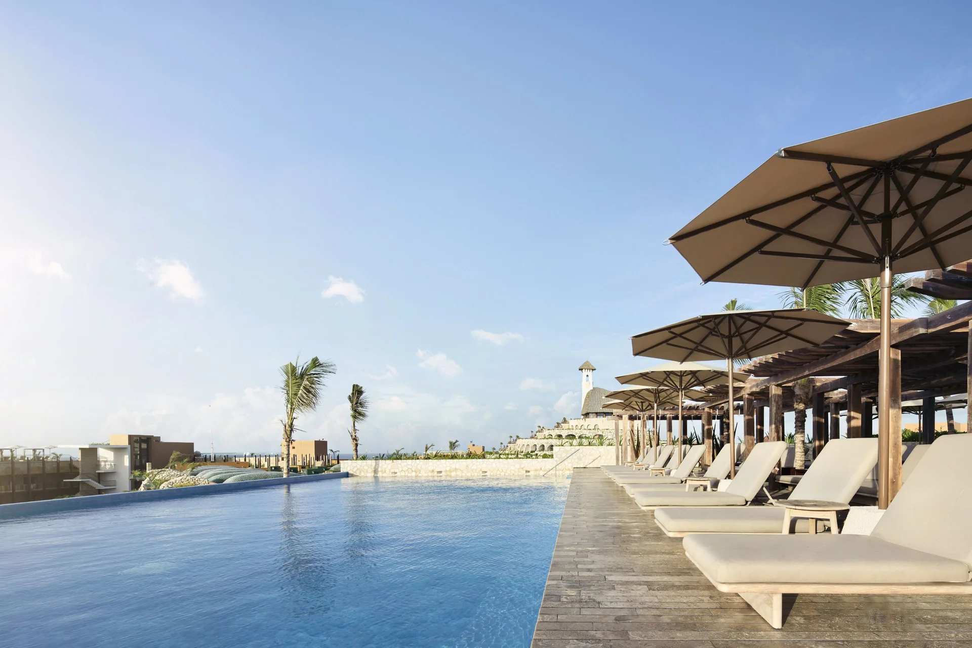 Infinity pool deck with rows of loungers and umbrellas at Hotel Xcaret Arte.