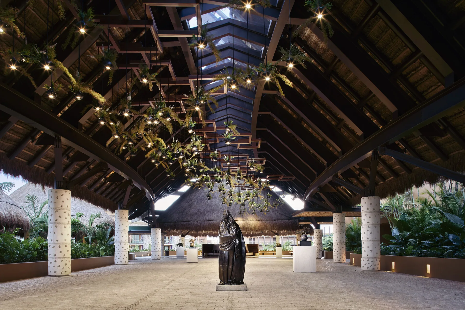 Open-air lobby pavilion with sculpture and hanging plants at Hotel Xcaret Arte.