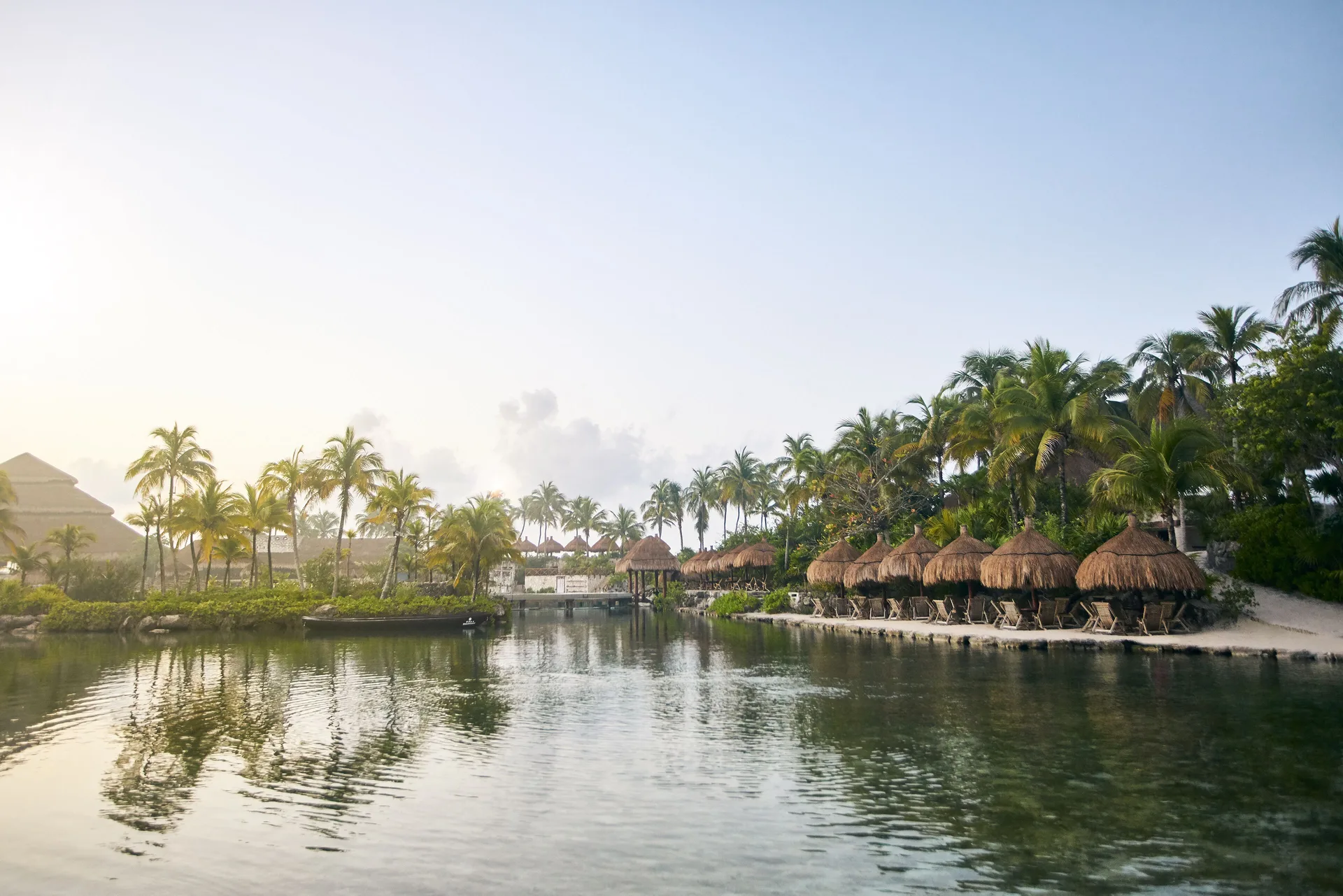 Palm-lined lagoon with thatched shade huts and loungers at Hotel Xcaret Arte.
