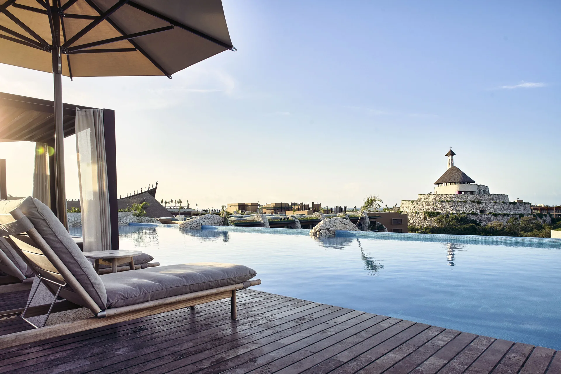 Poolside daybed and infinity pool at sunset at Hotel Xcaret Arte.