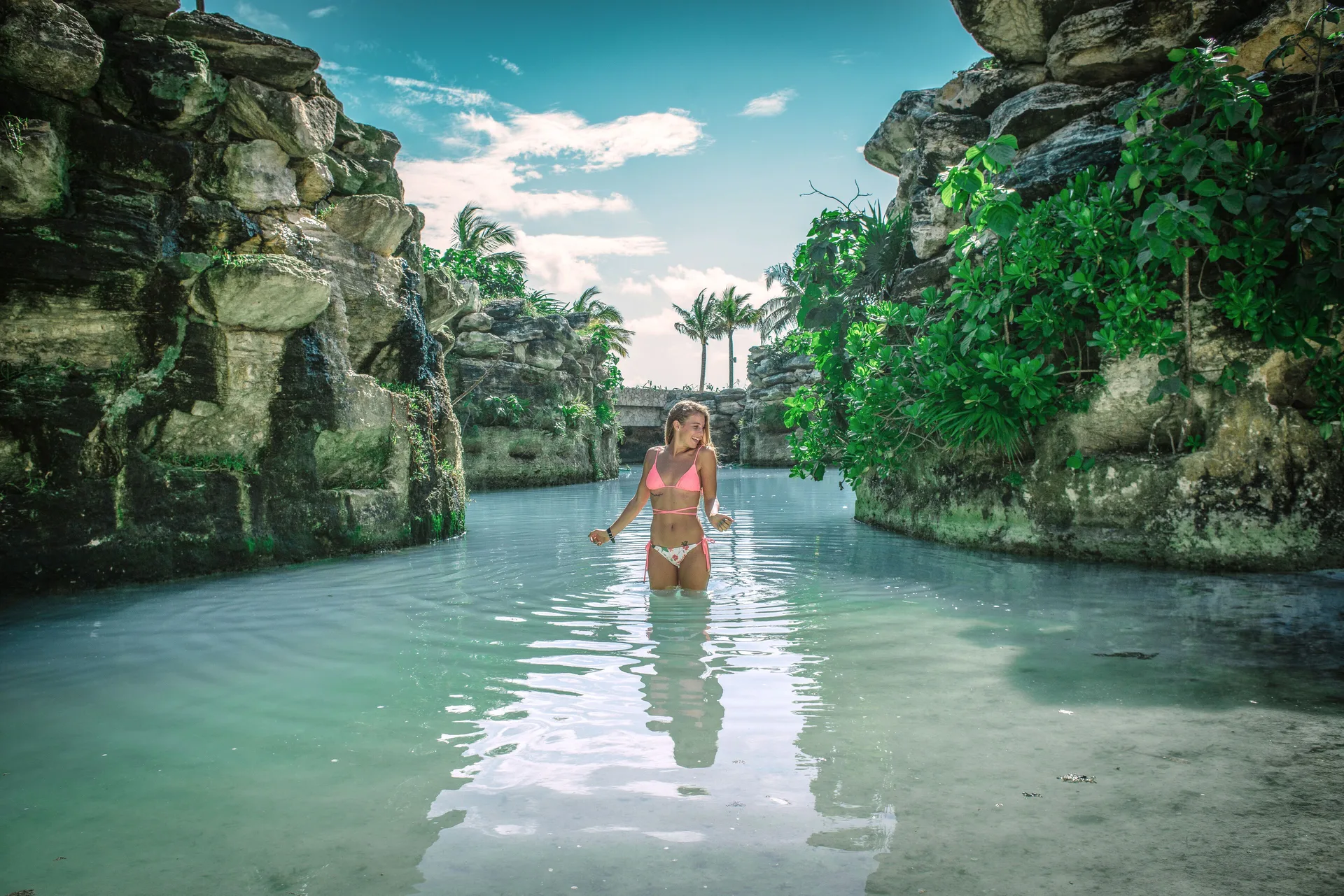 Guest wading through a turquoise rock-lined waterway at Hotel Xcaret Arte.