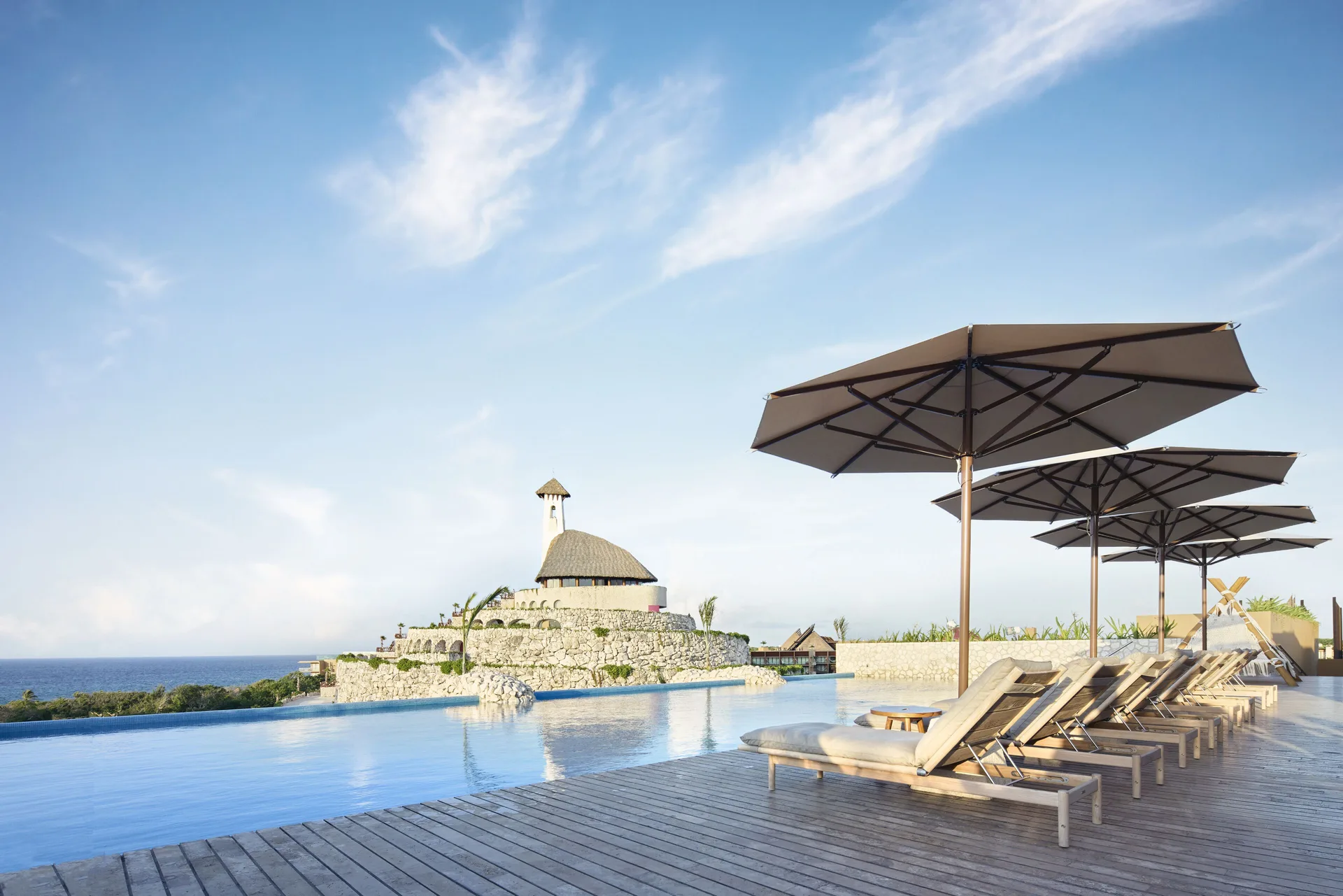 Rooftop infinity pool with loungers and umbrellas at Hotel Xcaret Arte.