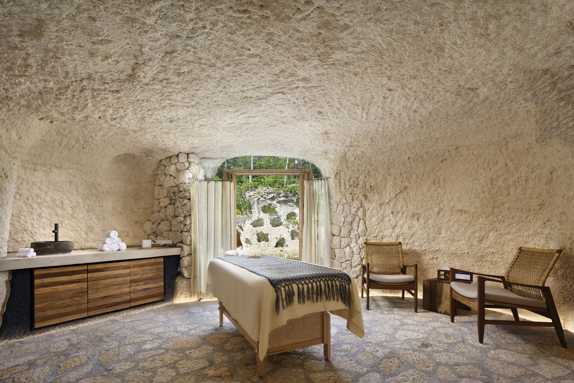 Single spa treatment room with stone walls and lounge chairs at Hotel Xcaret Arte.