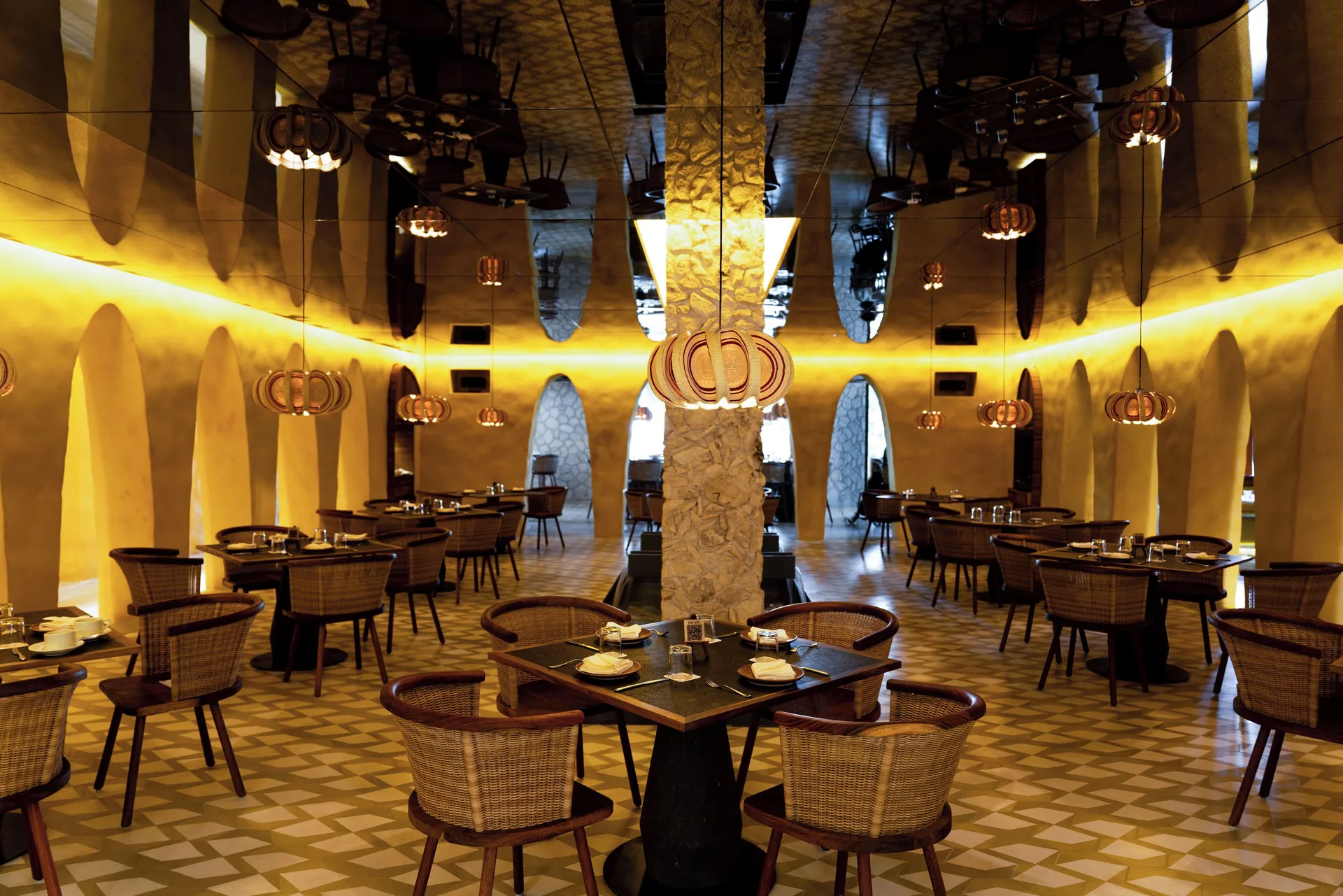 Warmly lit dining room with wicker chairs and arched walls at Hotel Xcaret Arte.