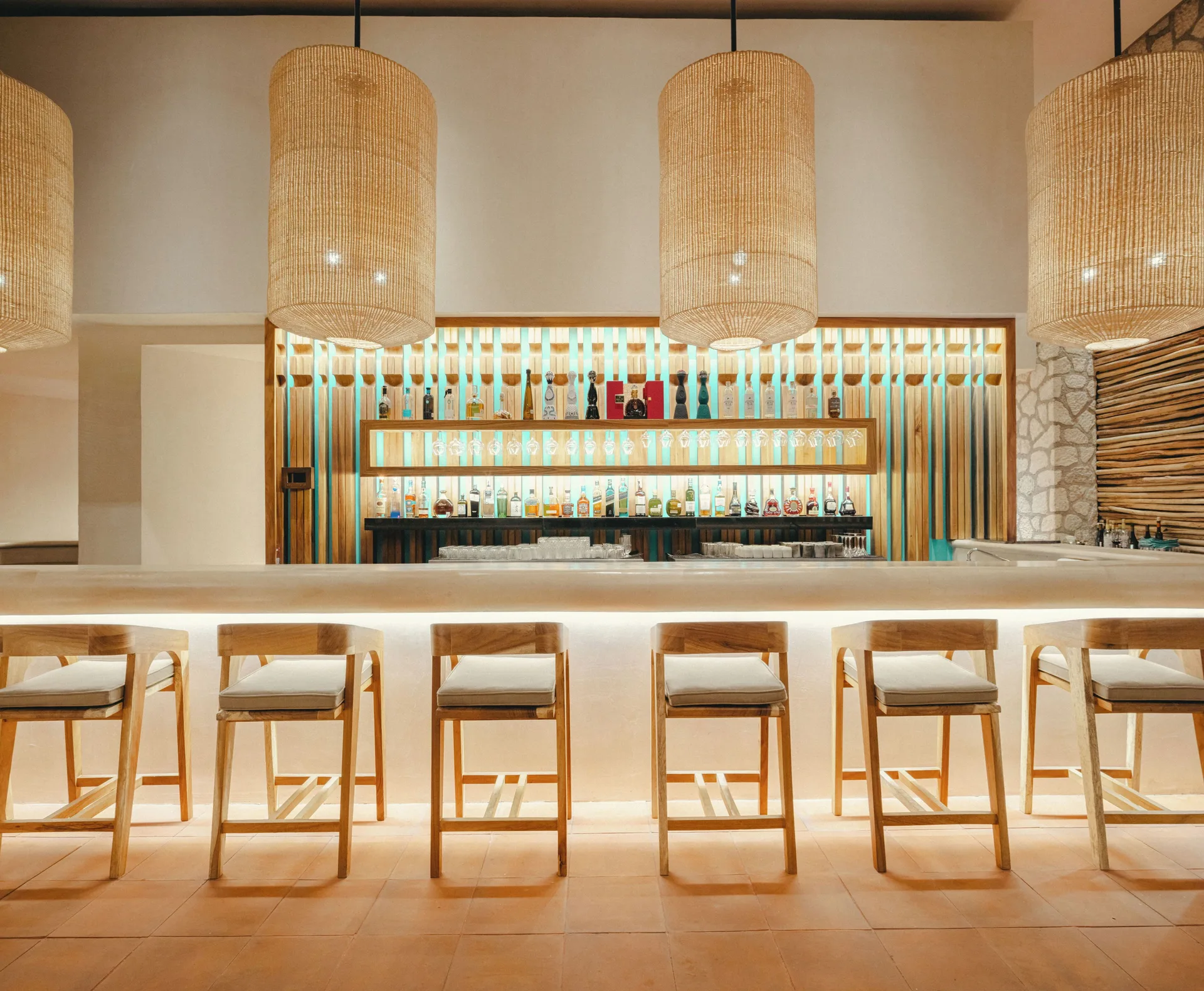 Bright bar with woven pendant lights, wood stools and backlit bottles at Hotel Xcaret Arte.