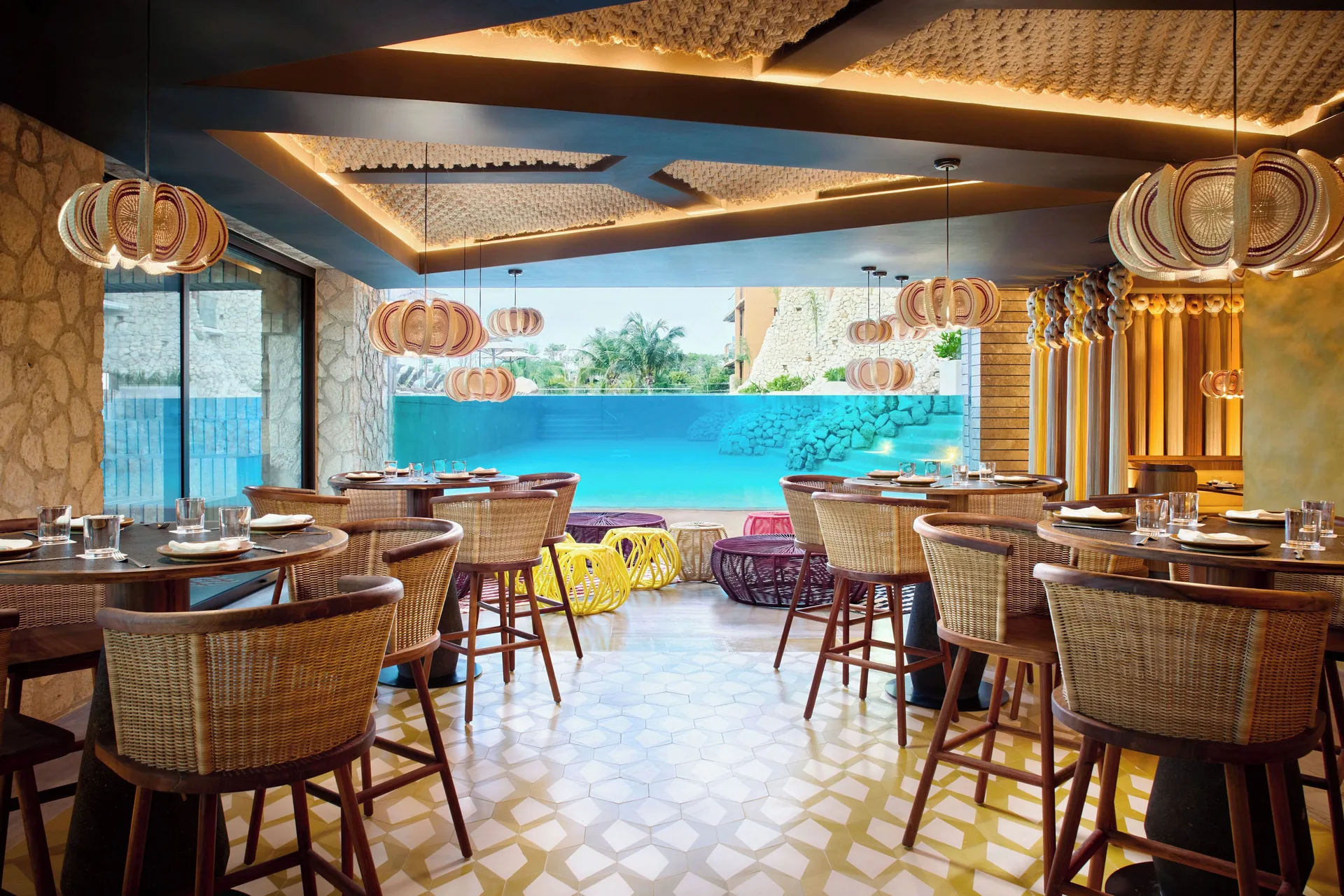 Bright restaurant dining room with wicker chairs and water view at Hotel Xcaret Arte.