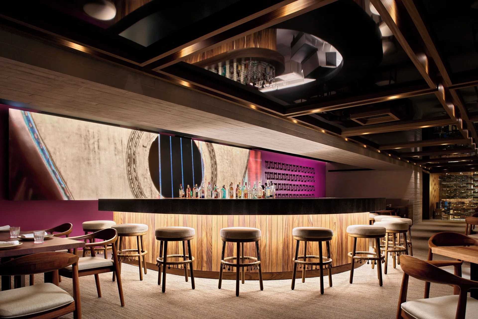 Modern bar with stools, bottle display and dark mirrored ceiling at Hotel Xcaret Arte.
