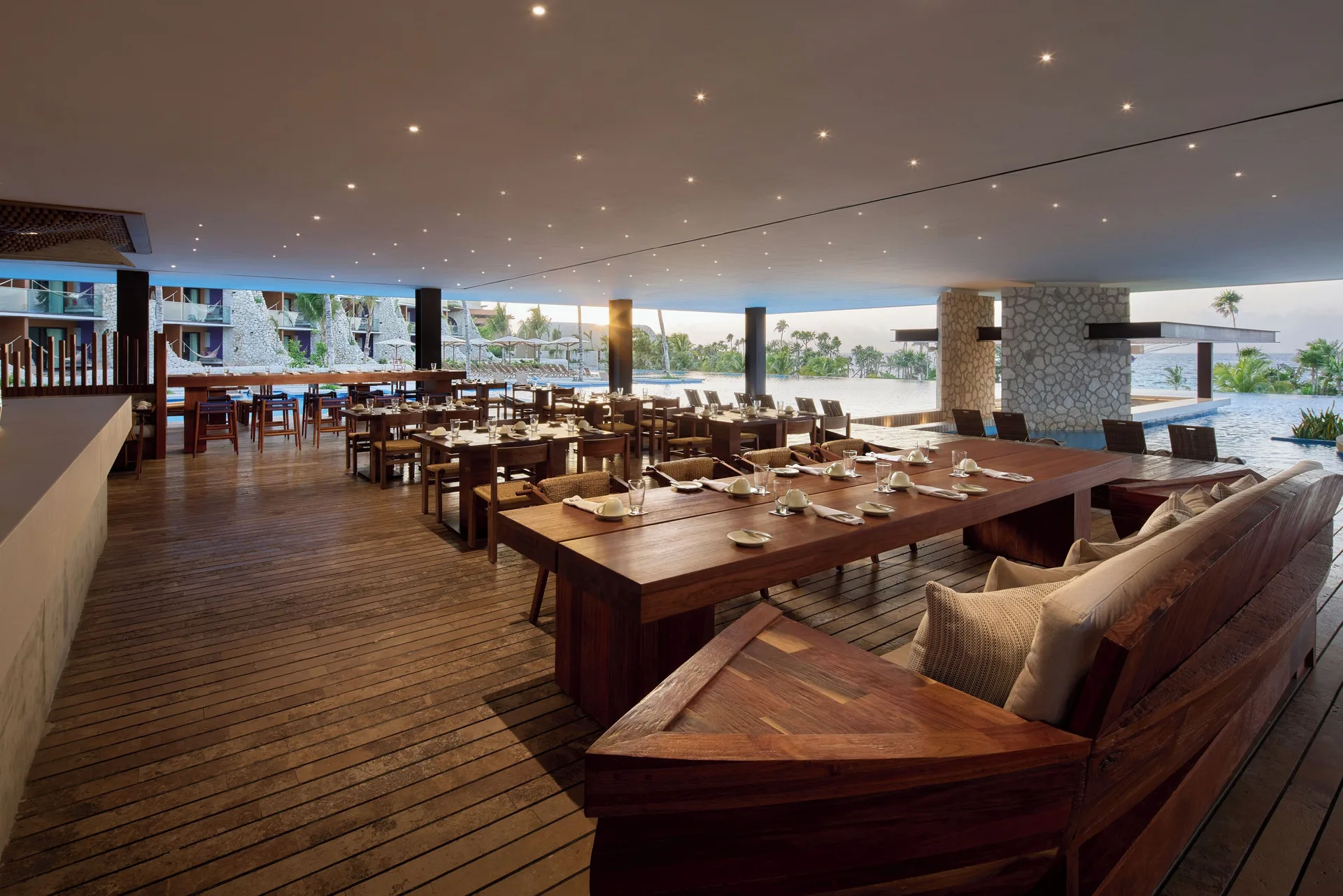 Open-air waterfront restaurant terrace with wood tables at Hotel Xcaret Arte.