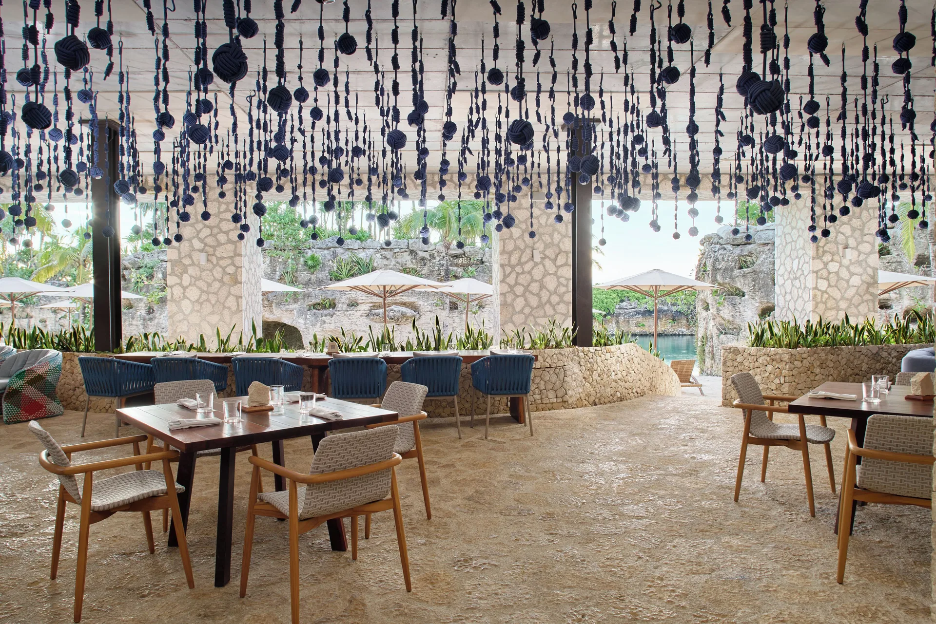 Restaurant terrace with woven chairs and dark hanging decor at Hotel Xcaret Arte.