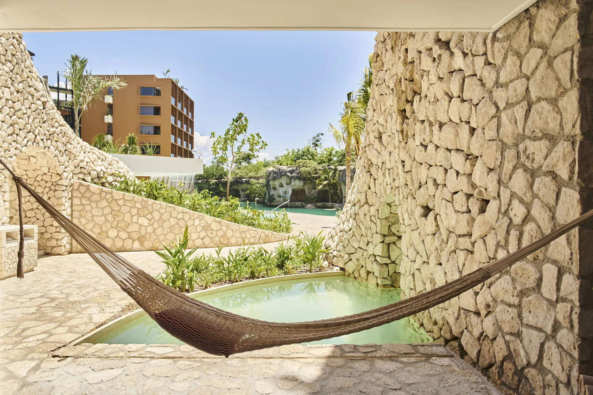 Swim-up room terrace with hammock and stone walls at Hotel Xcaret Arte.