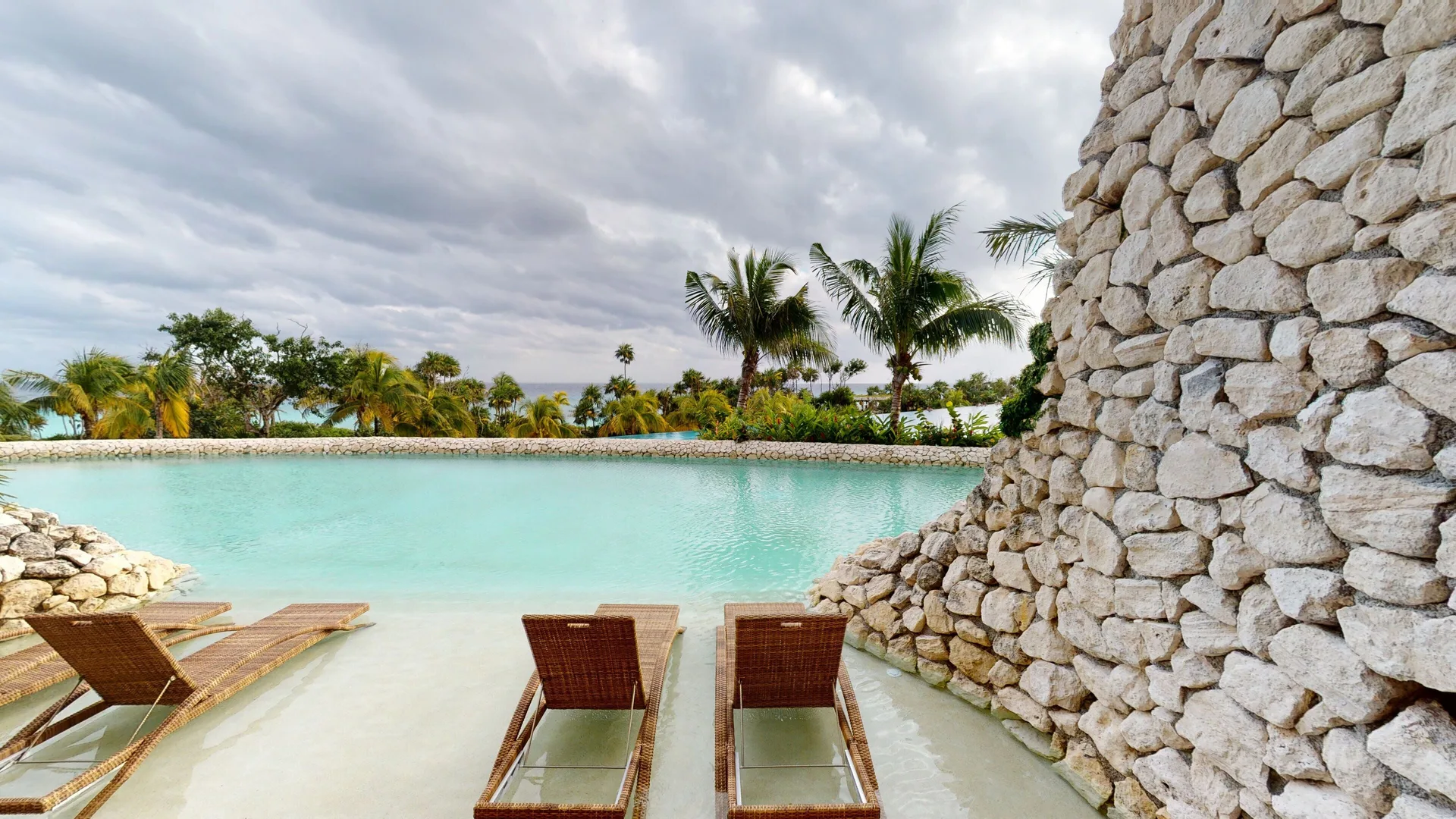 Oceanfront terrace lounge chairs by turquoise water at Hotel Xcaret Arte.