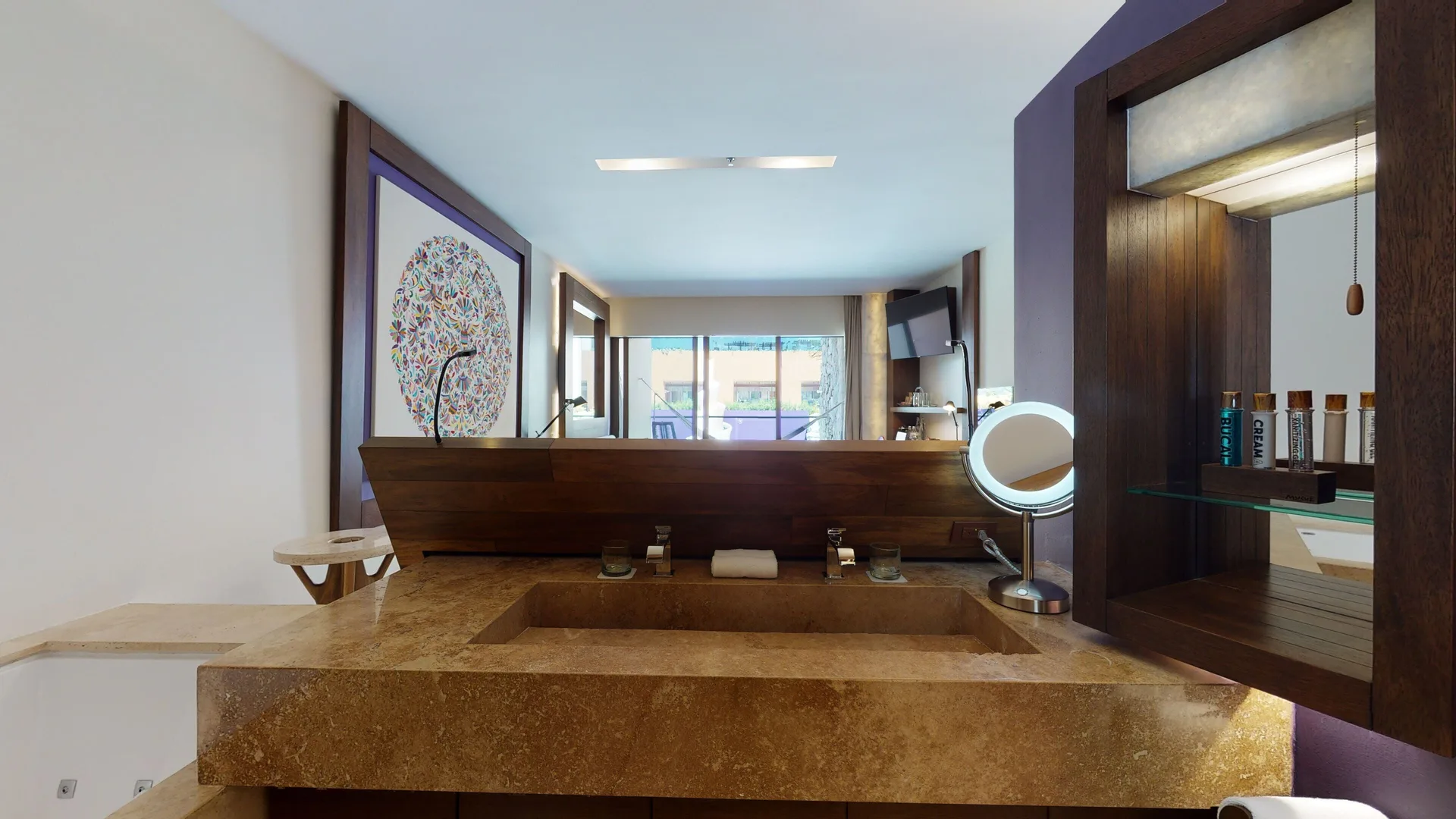 Garden Spa suite bathroom vanity at Hotel Xcaret Arte with stone sink, mirror, tub edge, and balcony beyond.