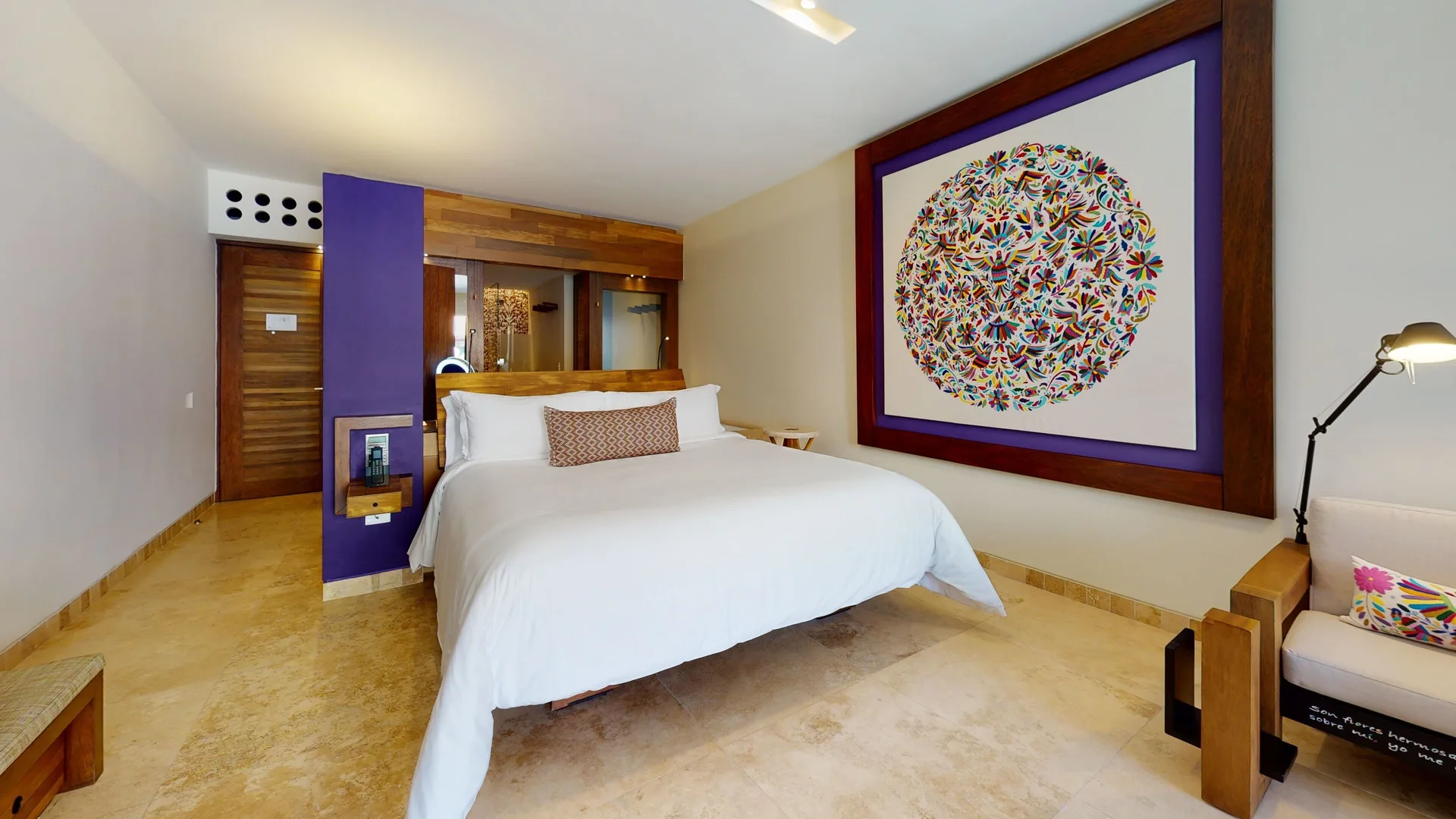 Garden Spa suite king bed at Hotel Xcaret Arte beside colorful artwork and a cream lounge chair.