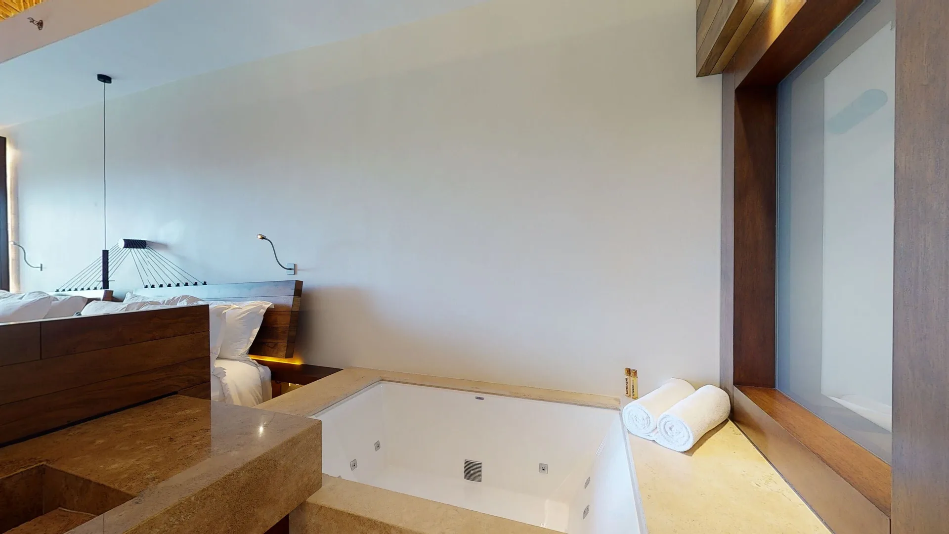 Garden suite soaking tub beside the bed and window at Hotel Xcaret Arte.