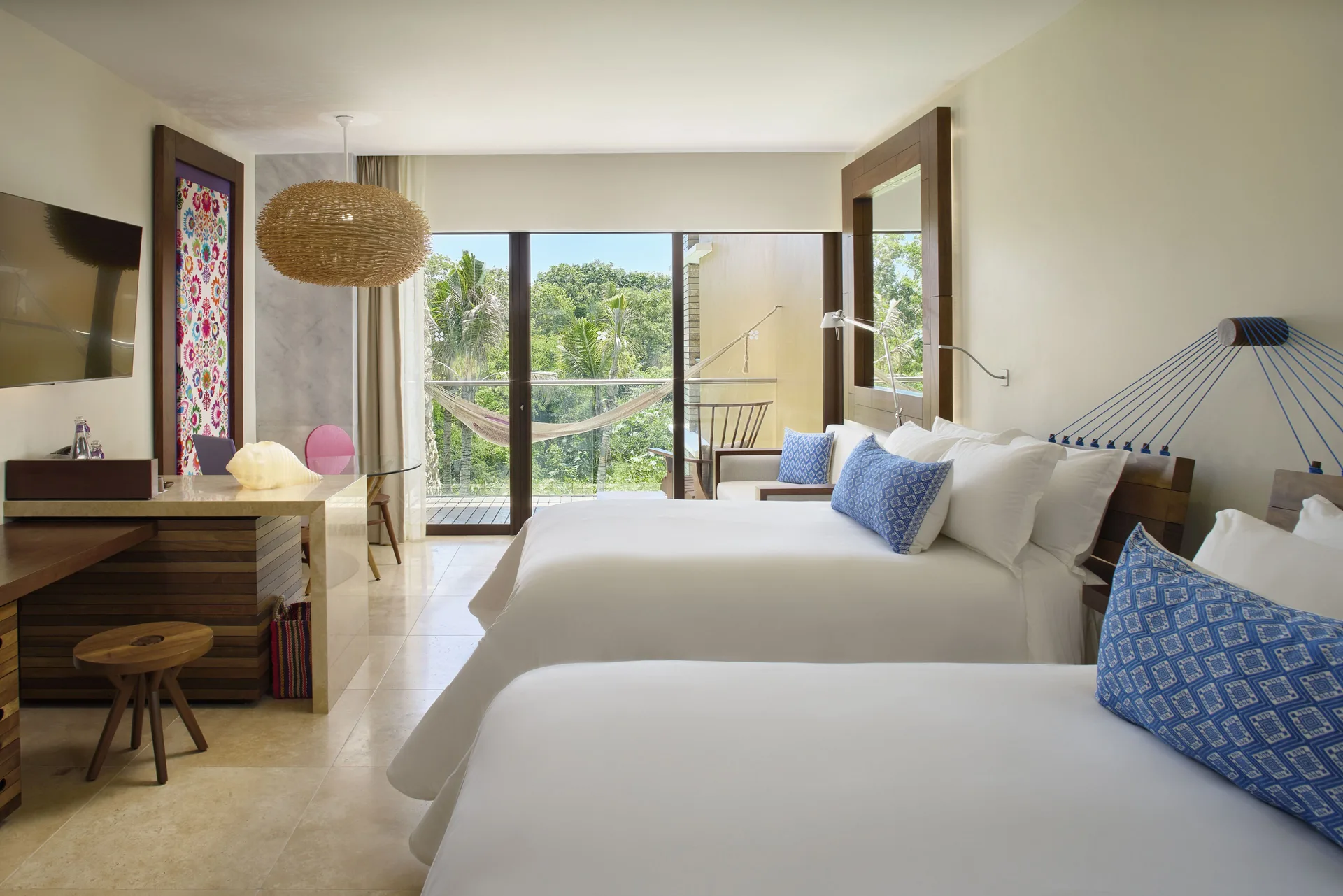Garden suite with two beds, desk, hammock balcony, and greenery at Hotel Xcaret Arte.
