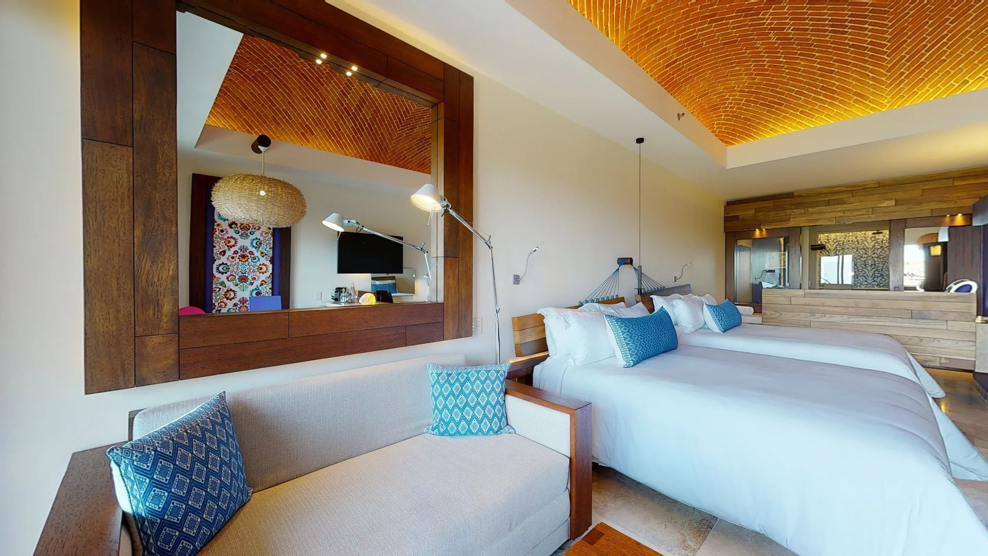 Garden suite with two beds, sofa, mirror, and brick ceiling at Hotel Xcaret Arte.